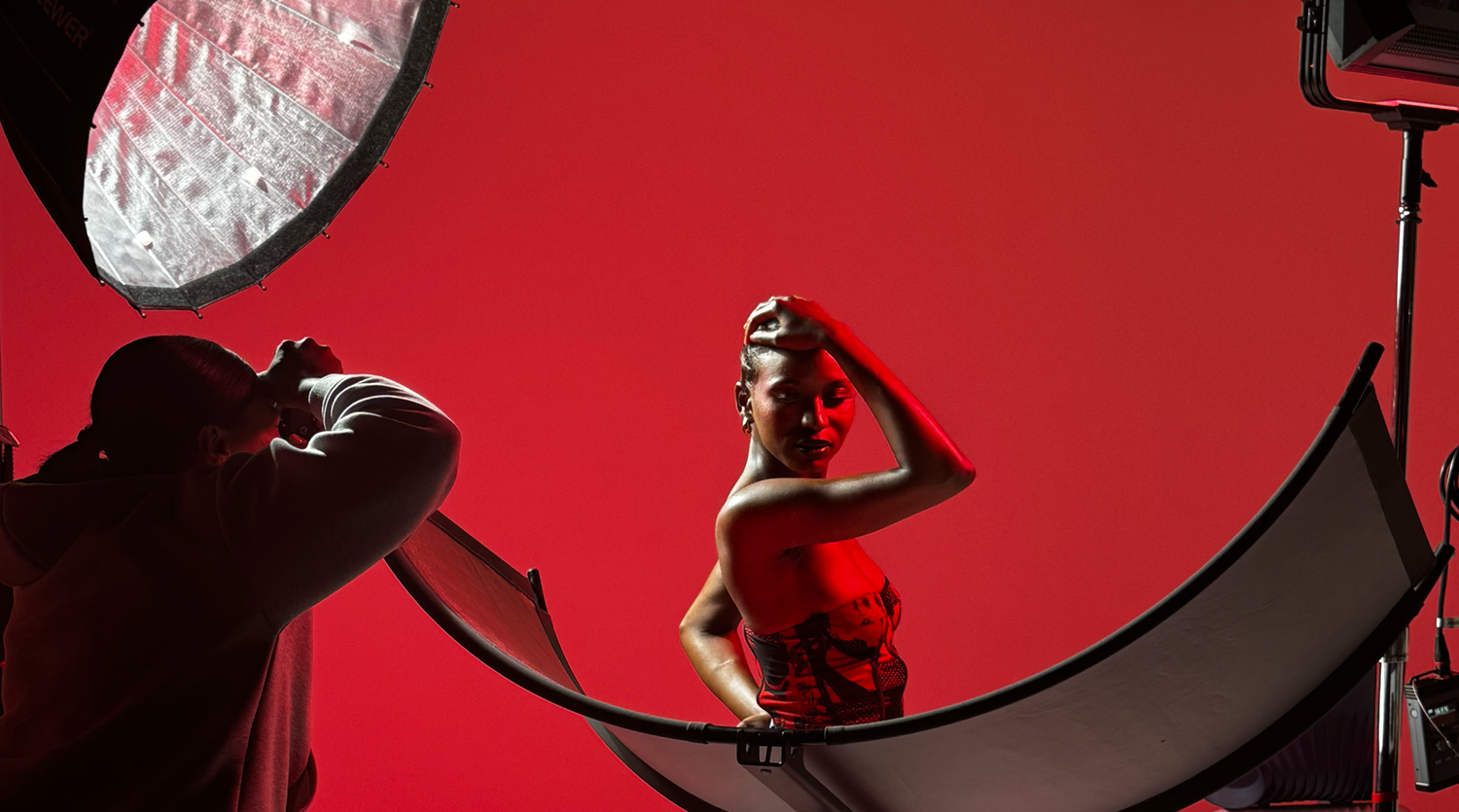 Silhouette of photographer shoots model in dramatic red lighting against circular backdrop setup.