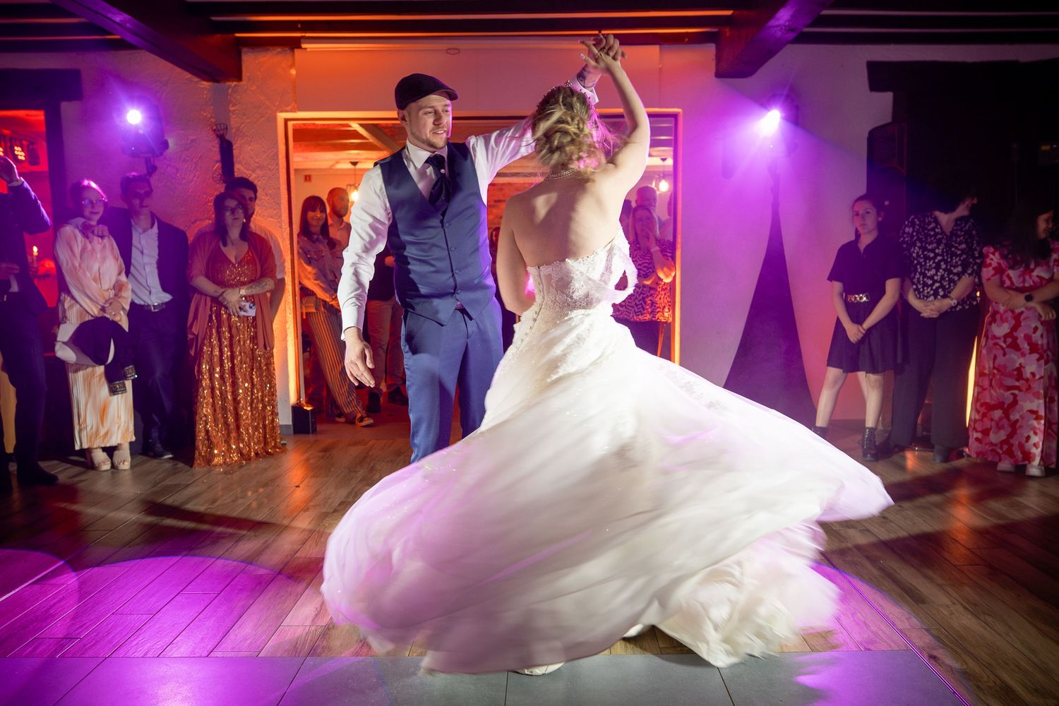 A dancing couple performs their first dance at a wedding reception under purple lighting in an event venue.