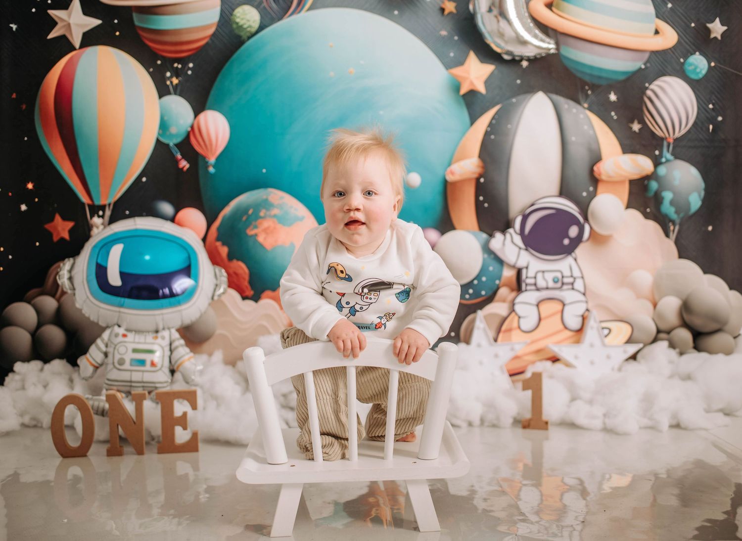 First birthday photoshoot with space-themed backdrop and white chair.