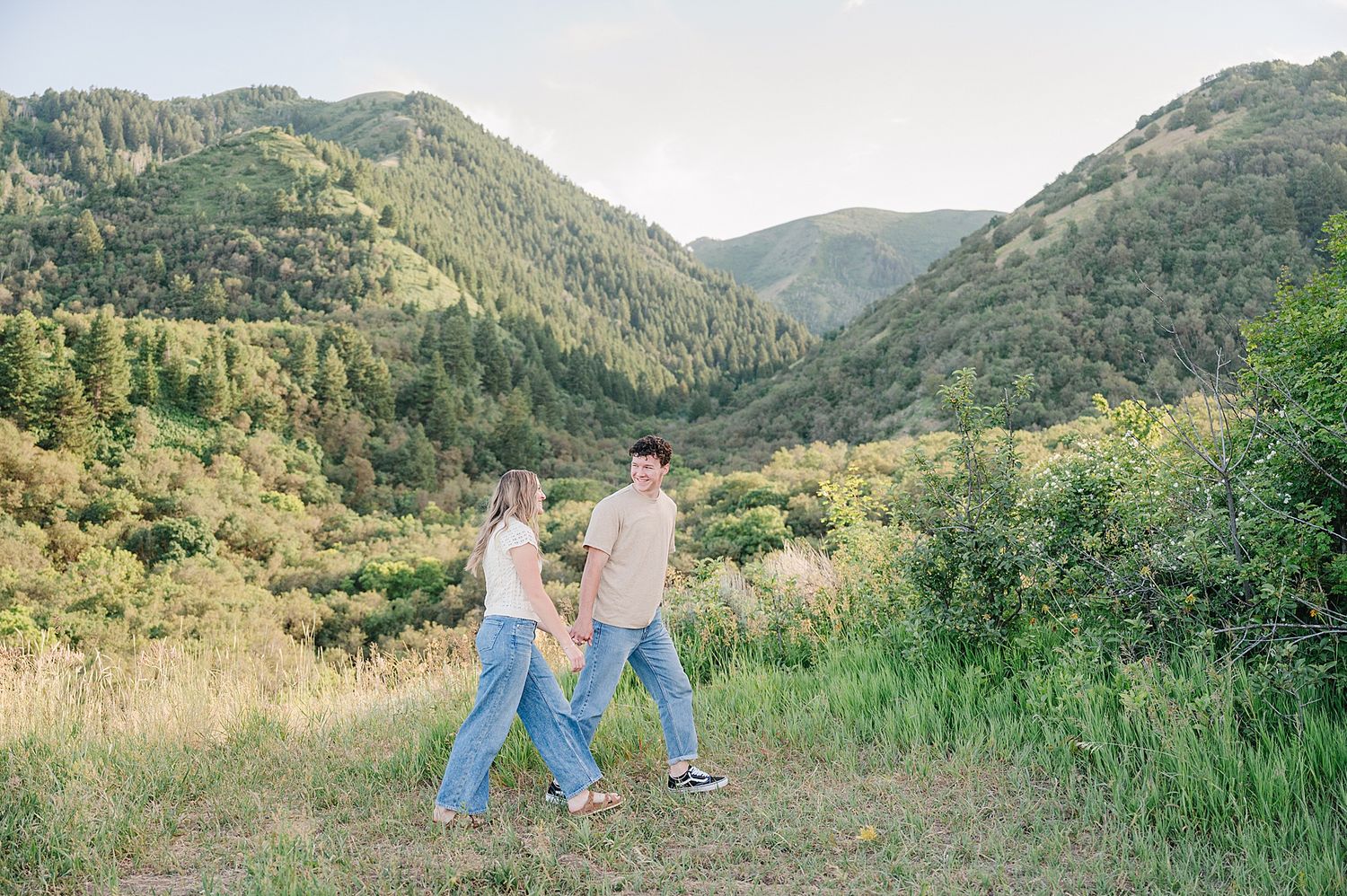 Couple walking hand in hand through a scenic mountain valley with lush greenery.