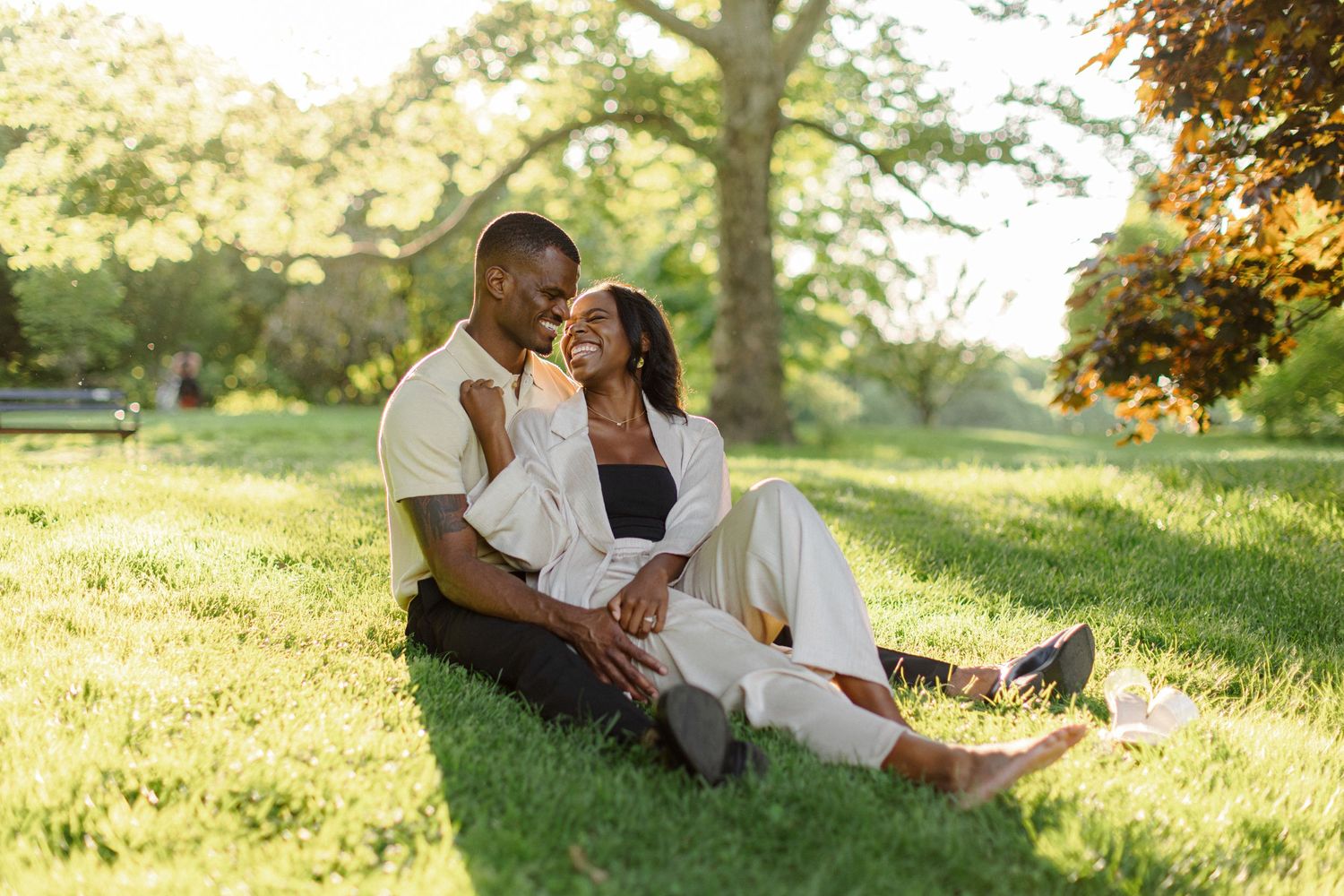A couple shares a tender moment while sitting together on grass in a sunlit park during golden hour.
