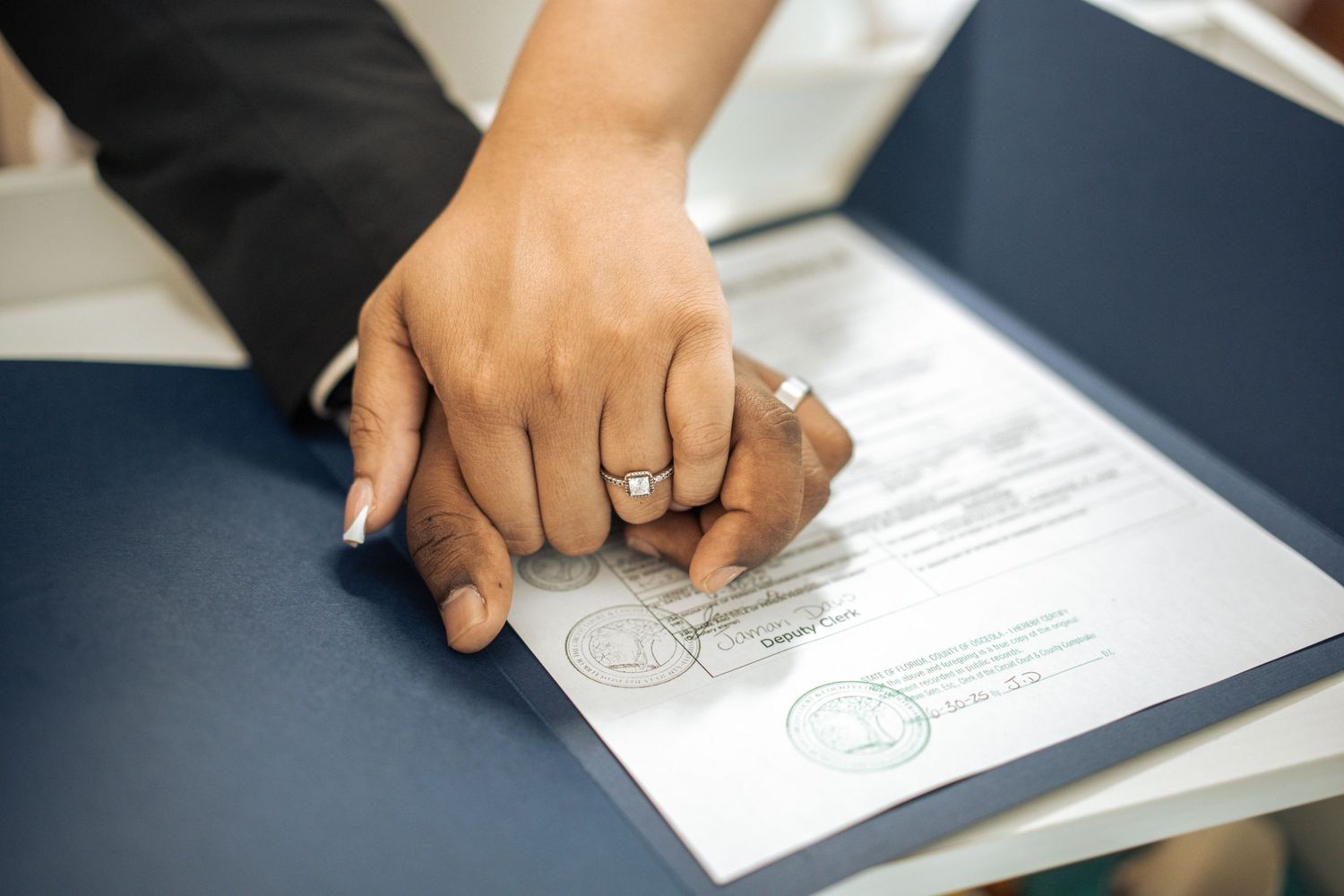 Close up of hands showing off an elegant diamond engagement ring with white manicured nails.