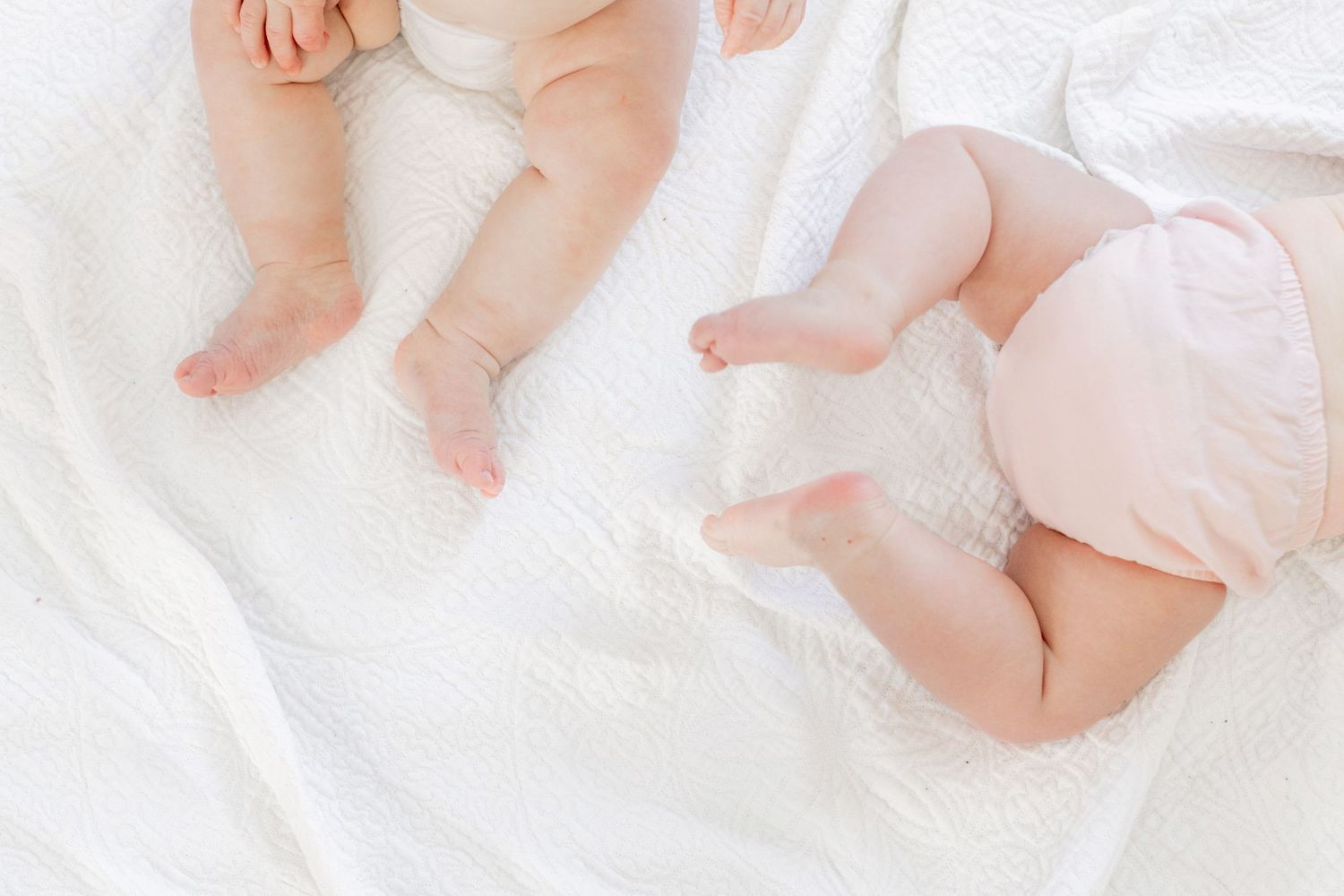Close up of baby feet and legs on white bedding with soft natural lighting.