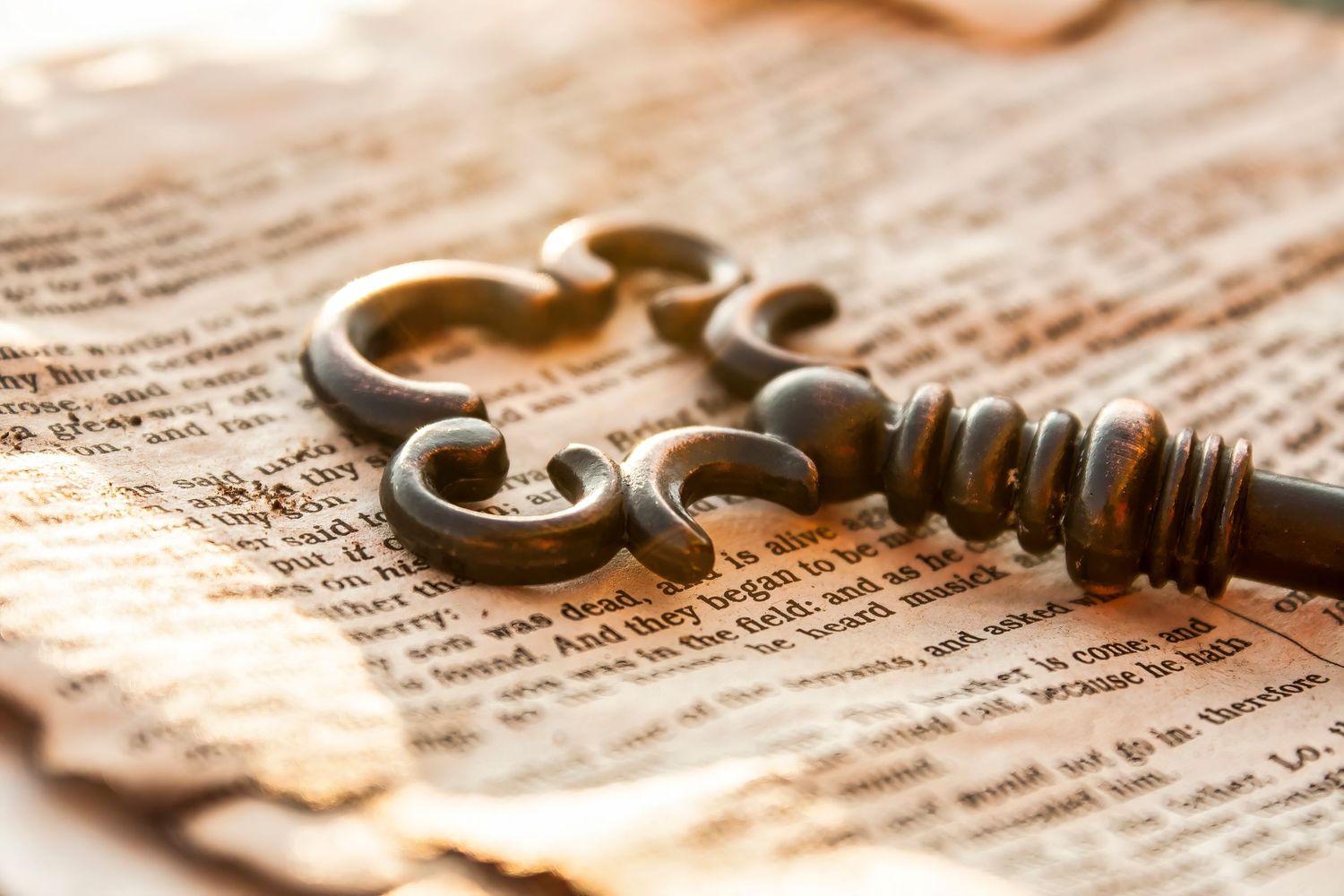 A vintage Key laying on on a page of a warn out bible with natural warm light all around.