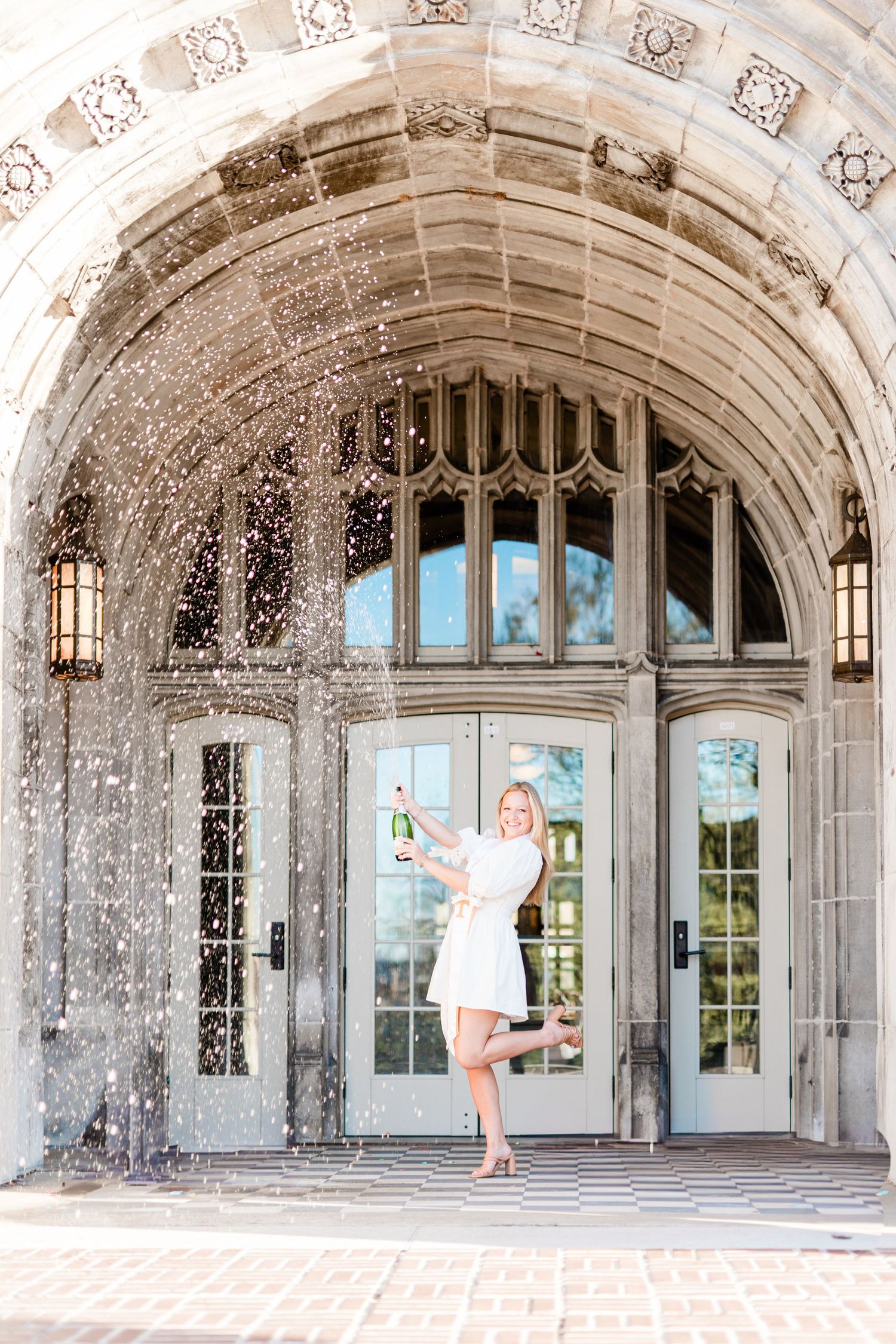 A ballet dancer performs an elegant pose in a grand stone archway with ornate Gothic architectural details.