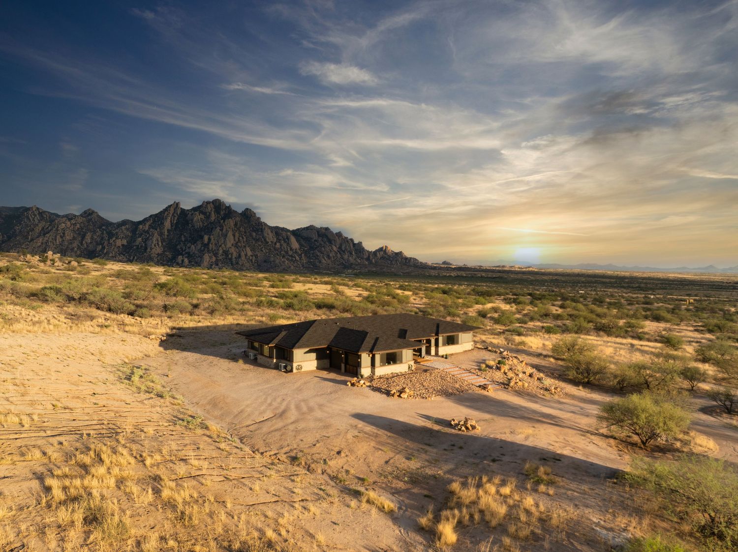 Panoramic desert landscape with rugged mountains and winding road under dramatic cloudy sky at sunset.