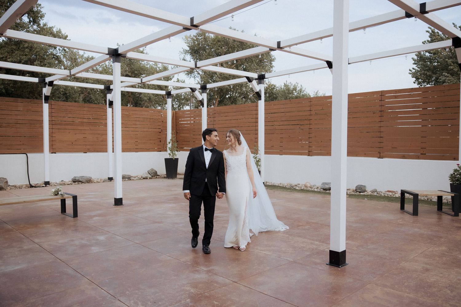 A couple holds hands outdoors during their wedding celebration with string lights glowing in the background.