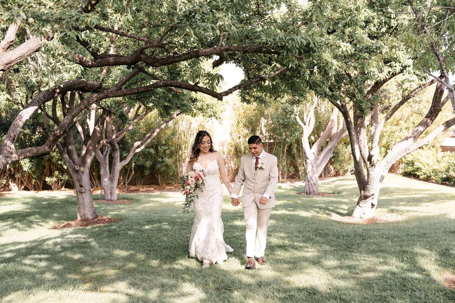A couple walks together on a scenic garden path surrounded by lush trees and dappled sunlight.