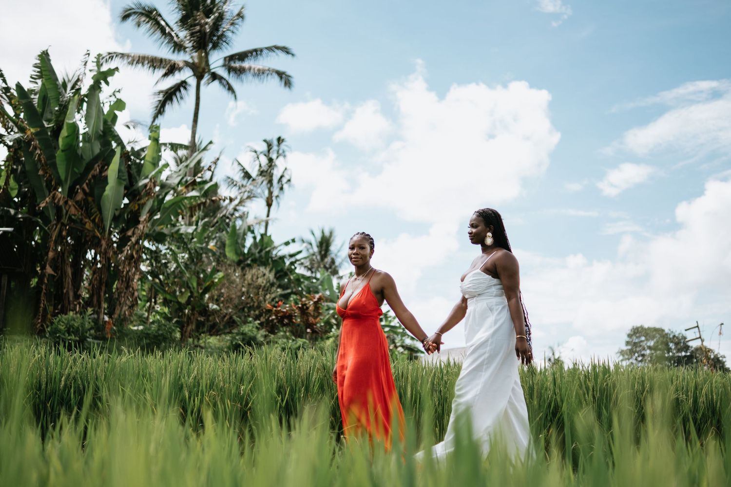 Two people walk through a lush tropical landscape with palm trees and green fields.