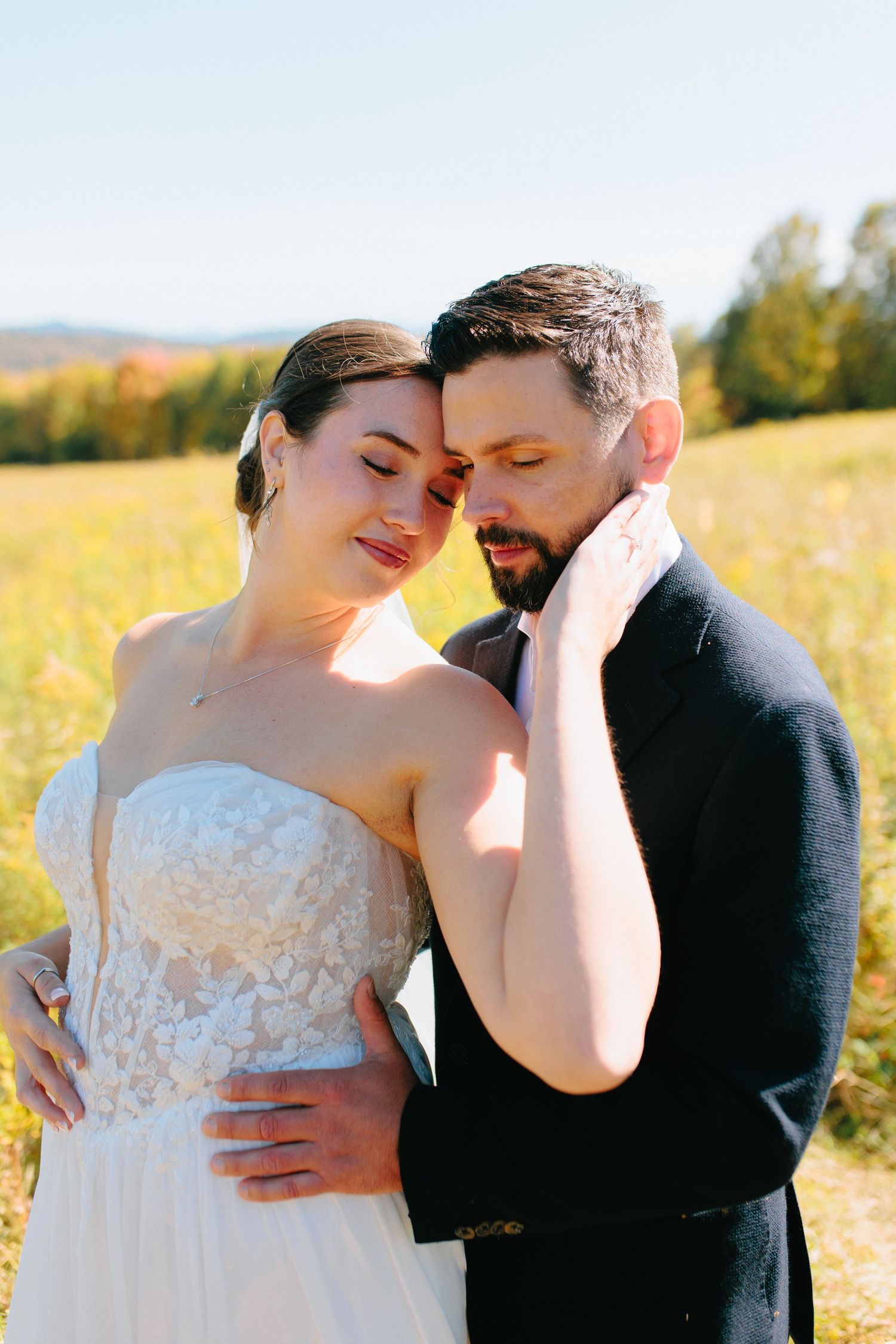 A romantic couple shares an intimate moment in a sunlit field of golden wildflowers during a wedding photo session.
