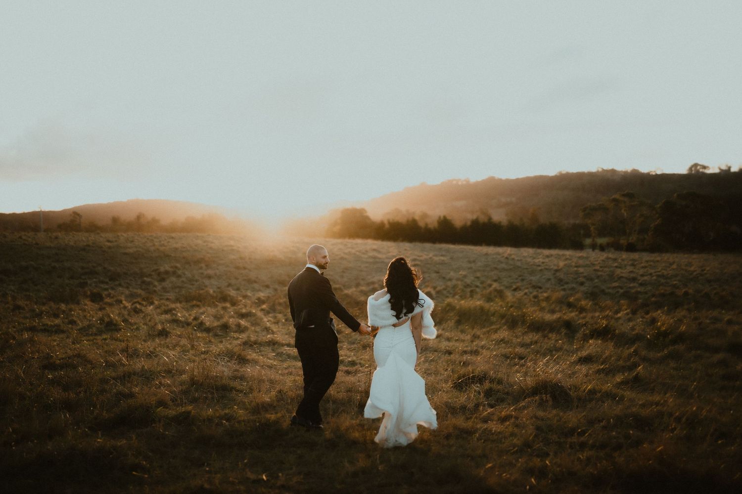A couple holds hands in a golden field during sunset creating a romantic silhouette.