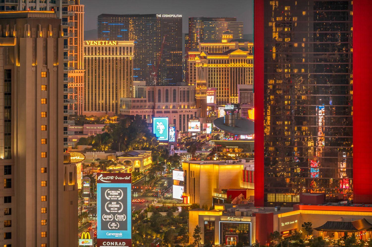 Aerial nighttime view of the illuminated Las Vegas Strip skyline with glowing casino hotels and billboards.