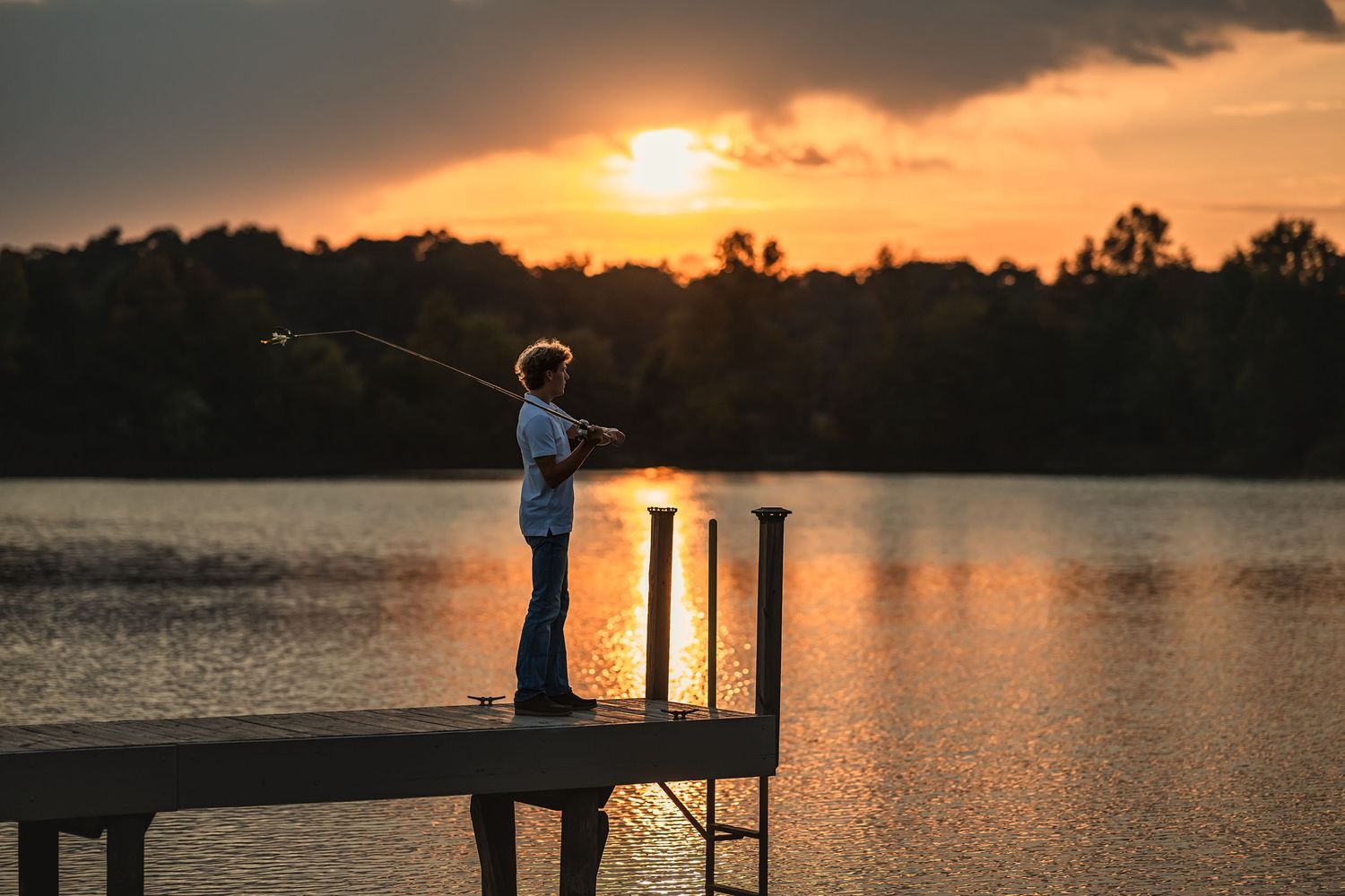 Backlit image of senior boy casting his fishing line off a dock at sunset for meaningful senior photos.