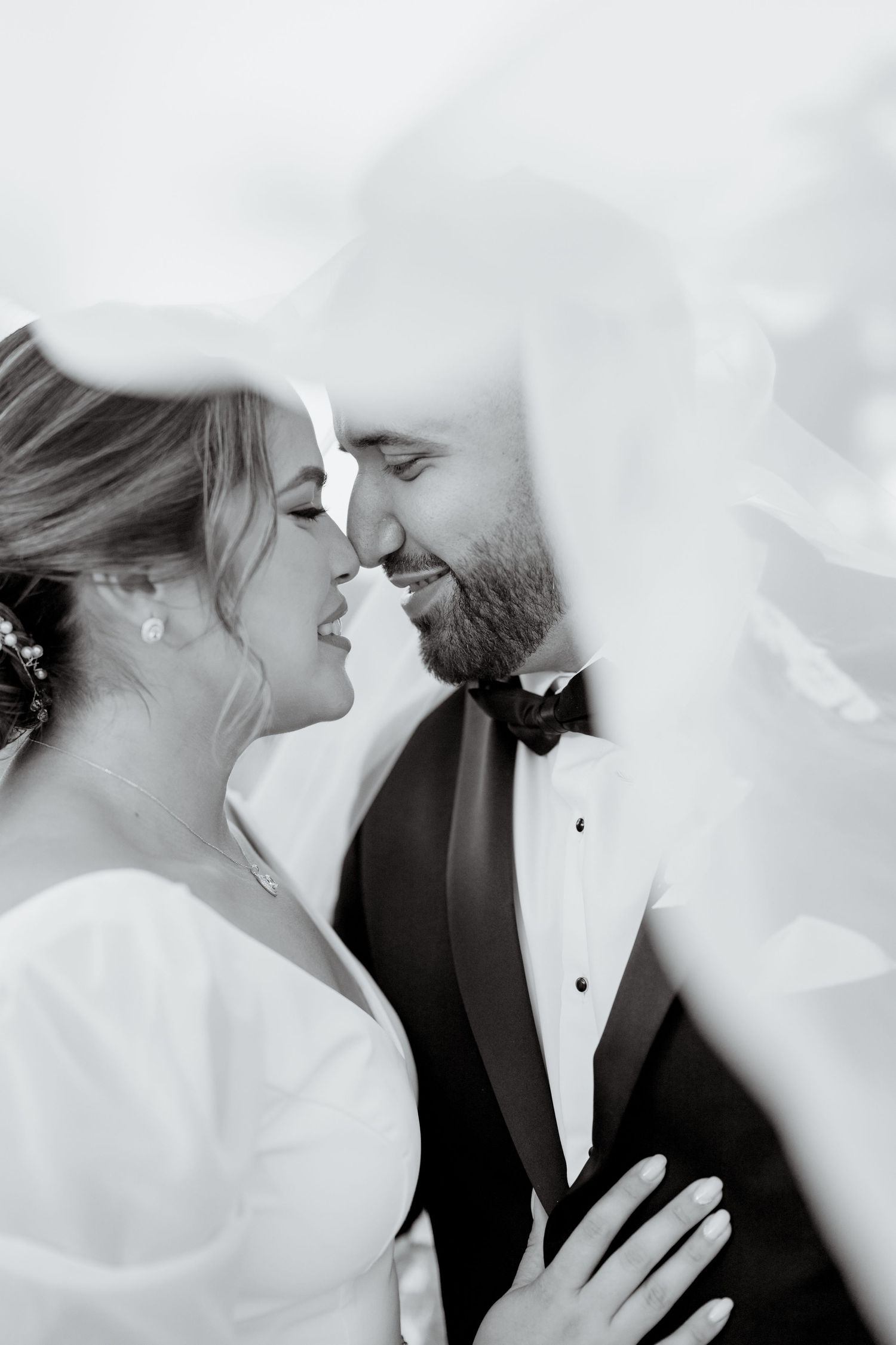 A romantic black and white wedding photo series showing intimate moments between a bride and groom under flowing veils.