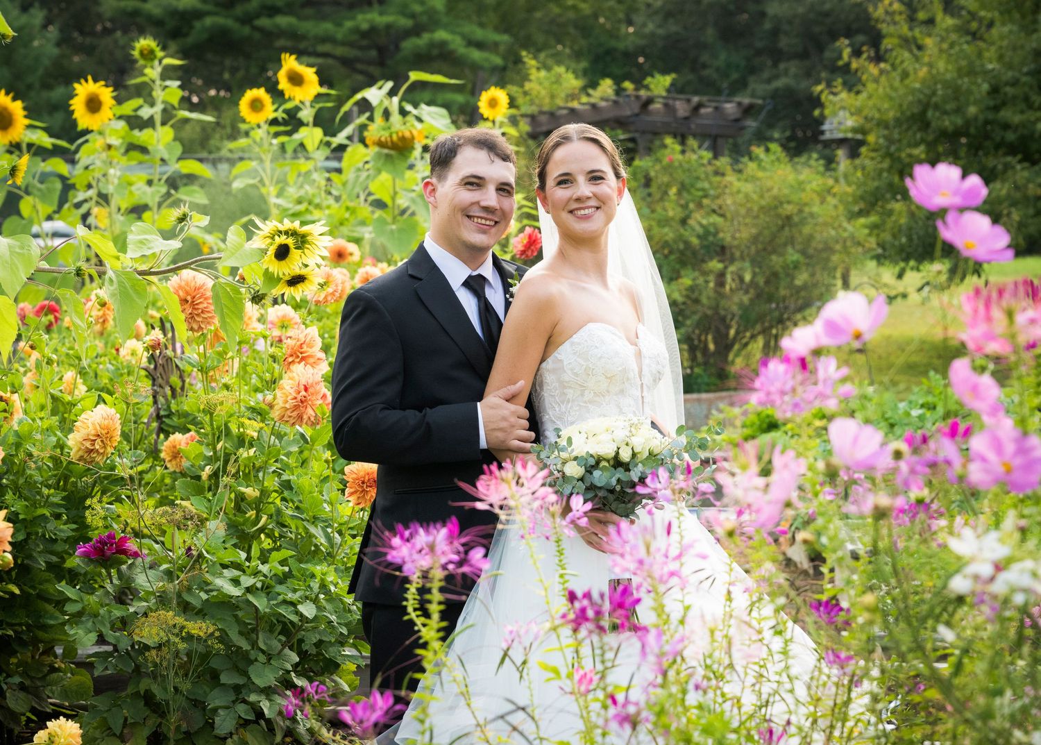 Newlyweds share an intimate moment outdoors with autumn foliage and rustic architecture in background.