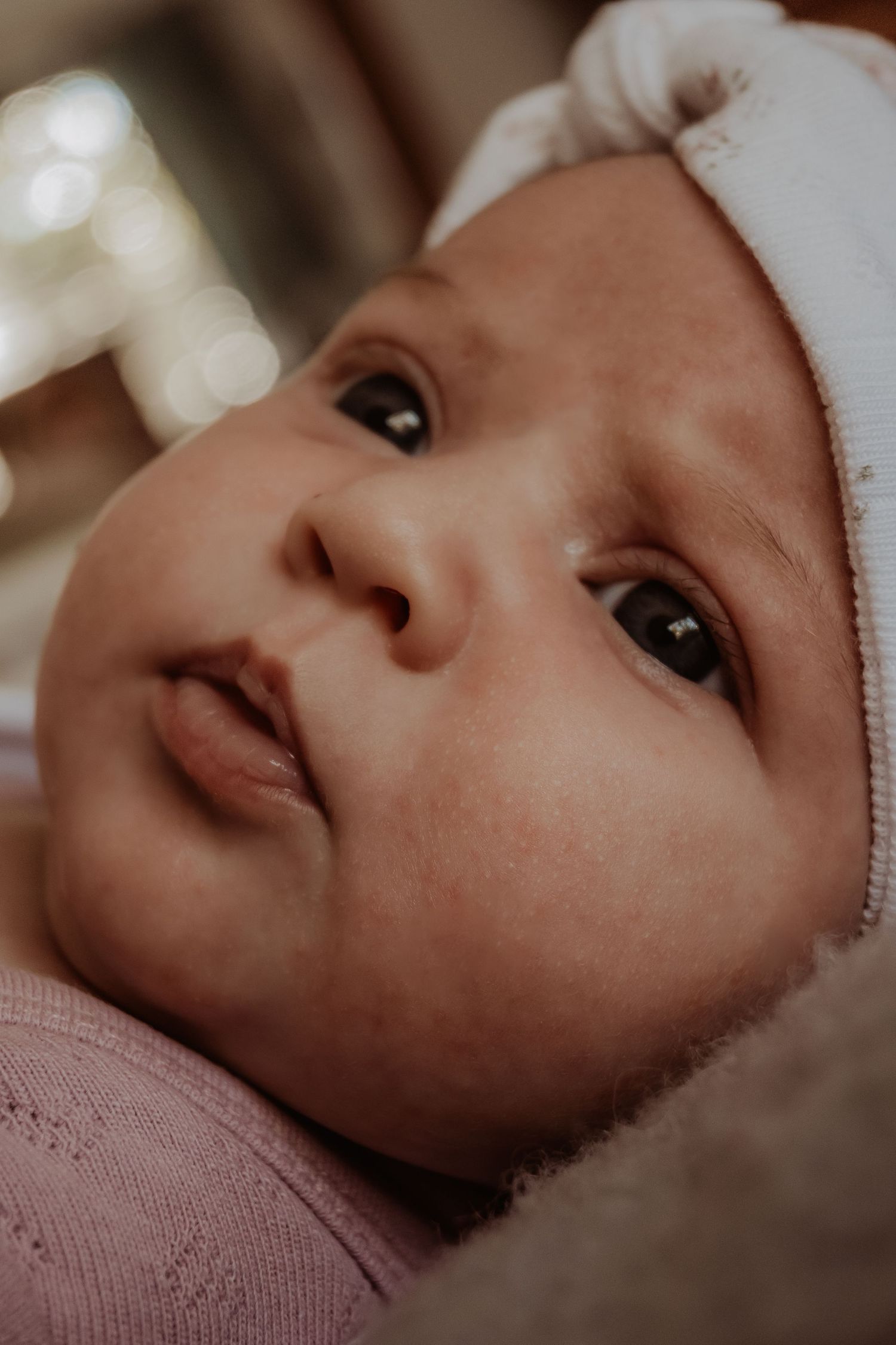 Close up view of a peaceful baby gazing upward while lying down, captured in soft lighting at a central coast newborn photoshoot.