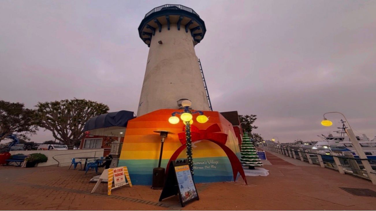 Panoramic sunset view of a beach boardwalk with glowing lampposts and palm trees silhouetted against the colorful sky.