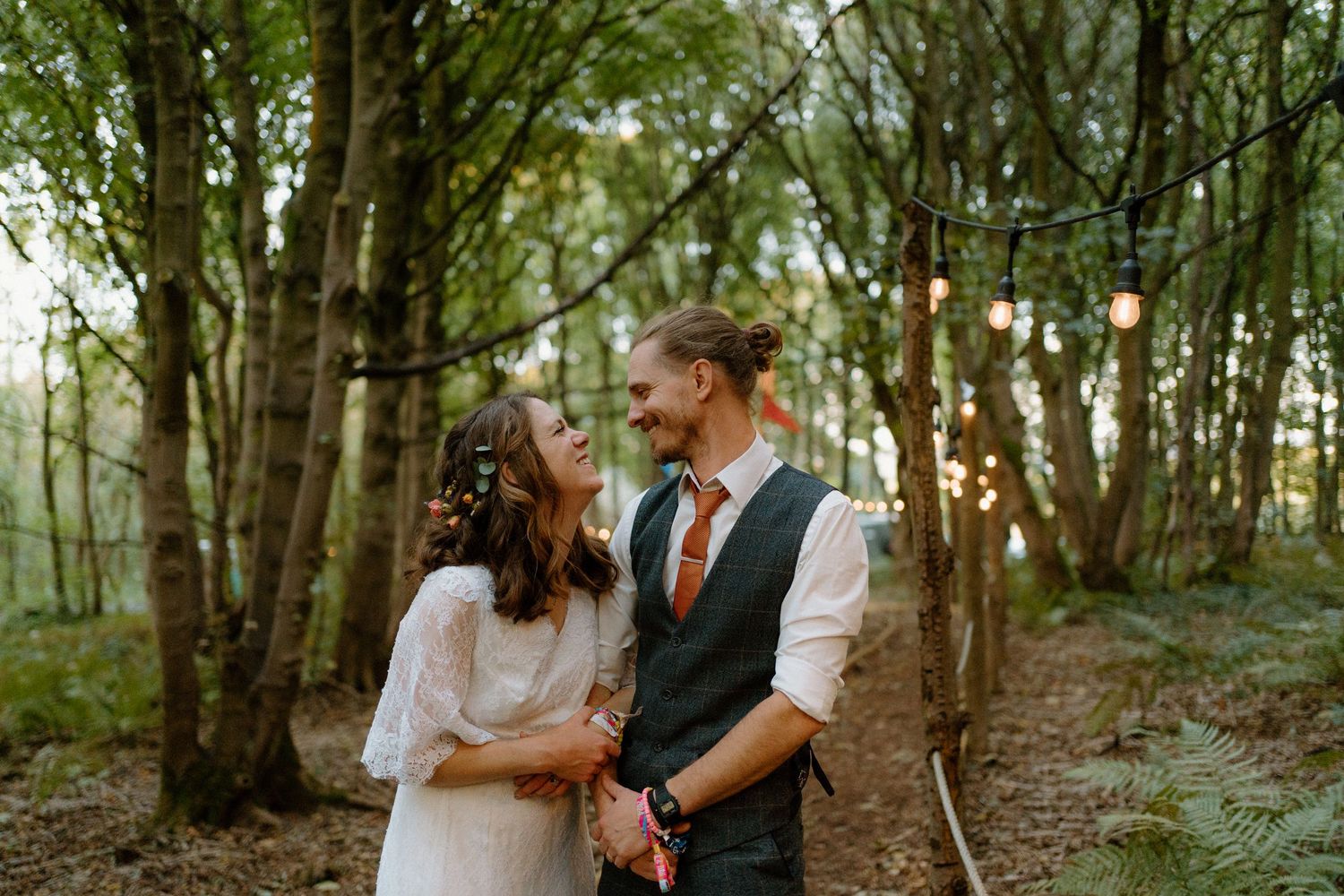 Sunlit outdoor wedding scene with couple standing by stone church surrounded by floral arrangements on a bright day.