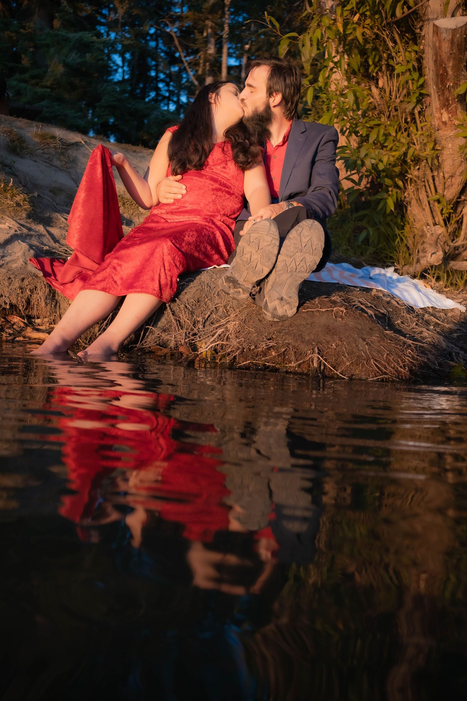 A person in a red dress sits at the edge of a reflective lake during golden hour creating a mirror-like reflection in the water.