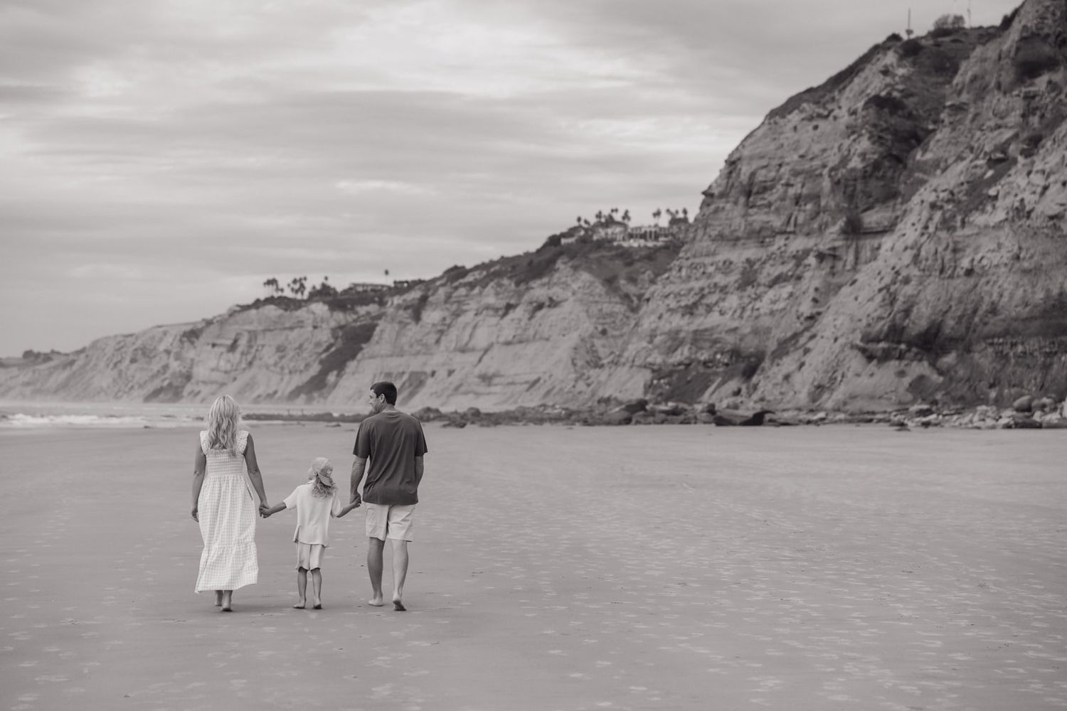 Family walking together on a misty beach with cliffs in the background at sunset.