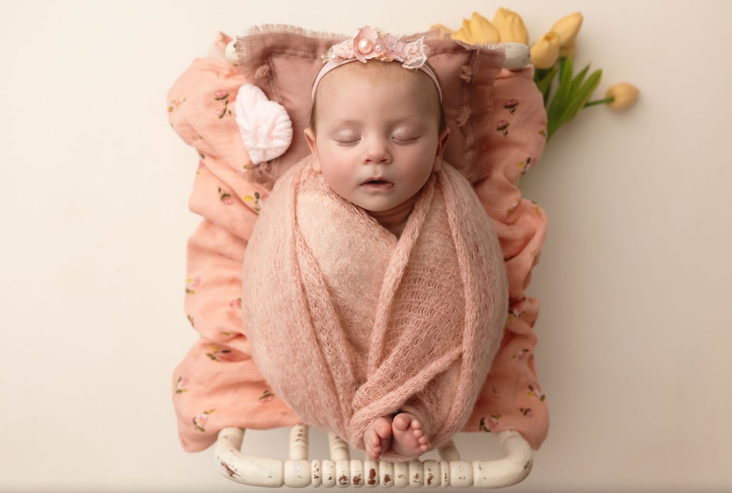 Pretty in pink newborn baby girl sleeps in spindle crib and is surrounded by tulips during a Spring newborn session in Charlottesville.