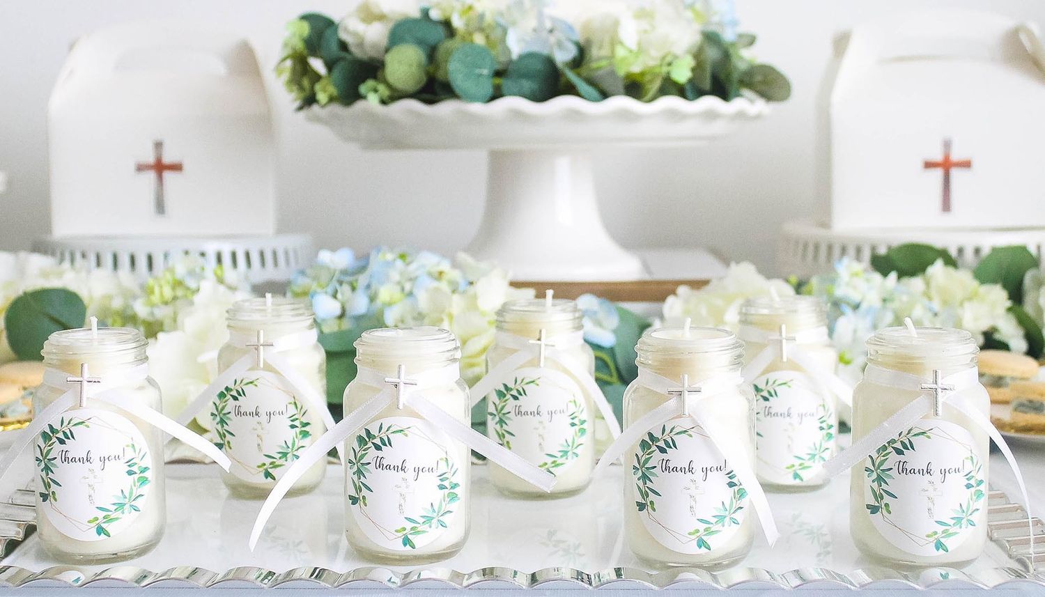 White ceramic mugs with green floral designs displayed in a row on a white surface with greenery accents.