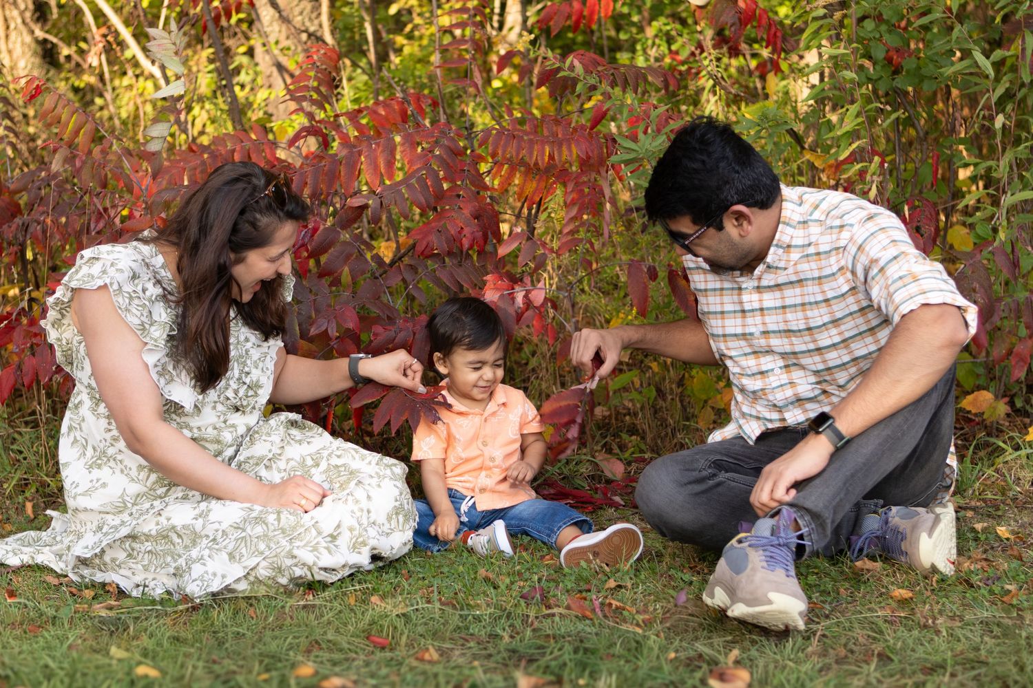 A family relaxes together on a blanket during an autumn outdoor photo session with red foliage.