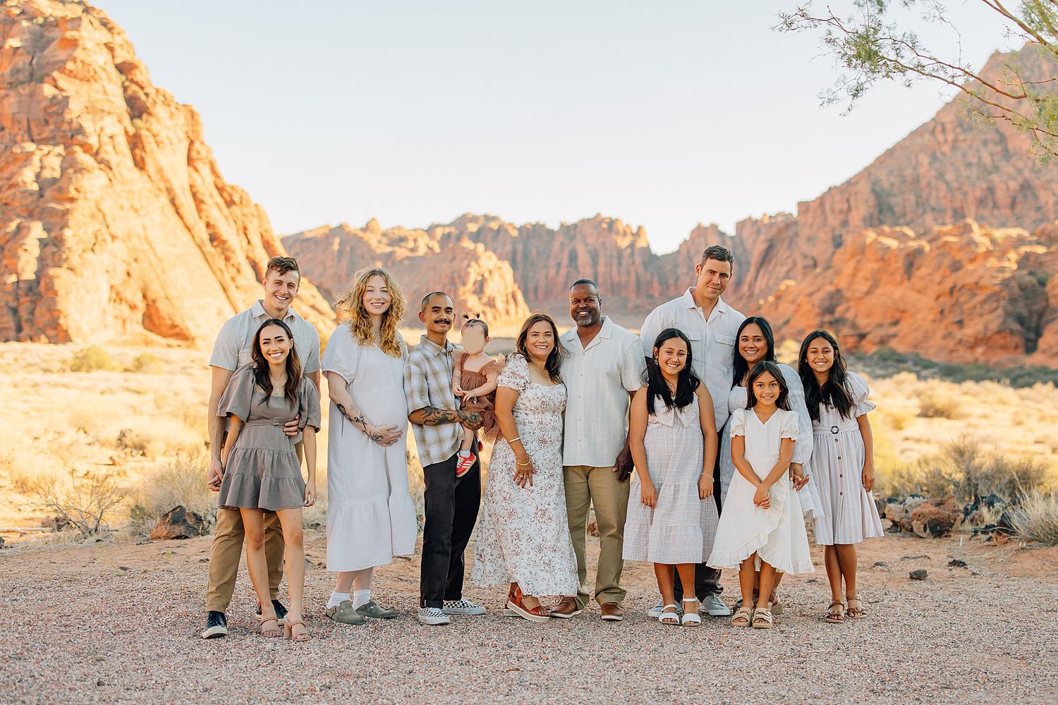 Family group poses casually on desert terrain with towering red rock formations in background.
