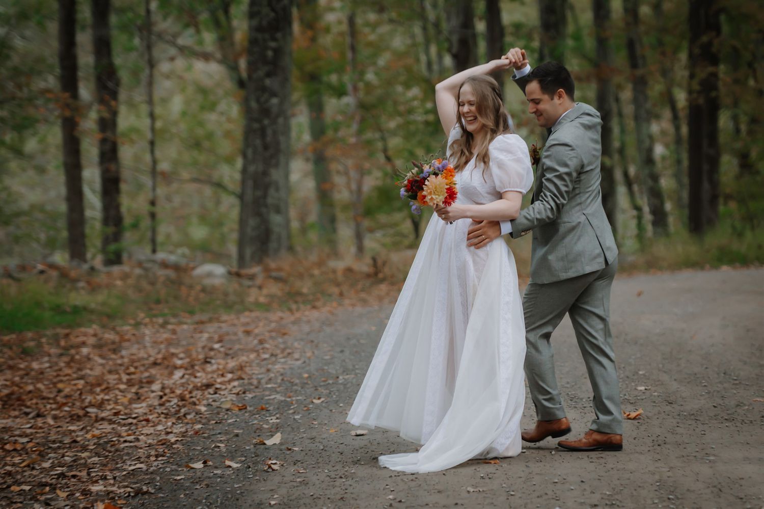 A couple walking together outdoors, with a bride in a white dress holding a colorful bouquet and a groom in a gray suit.