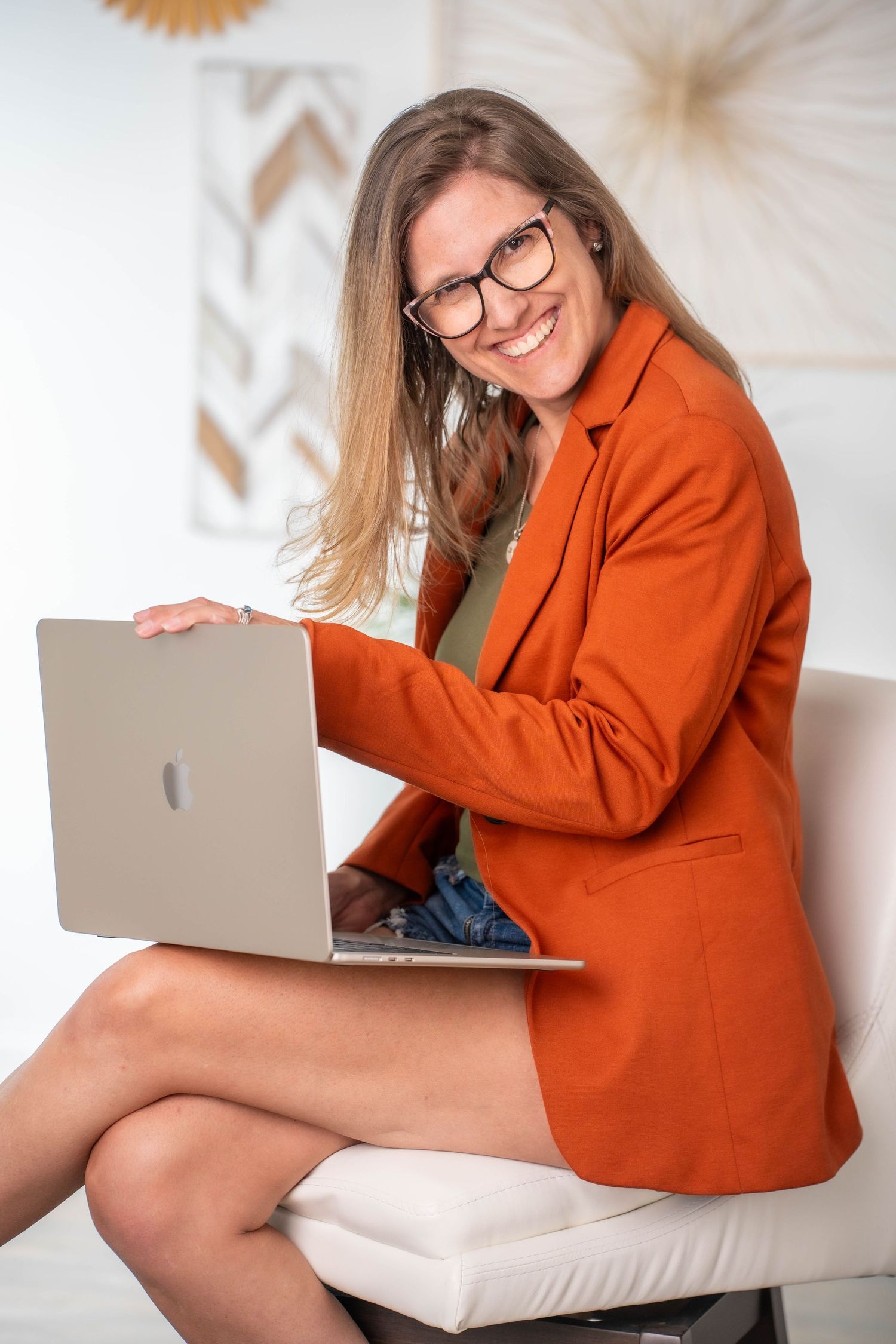 Professional in orange blazer working on laptop in modern office setting.