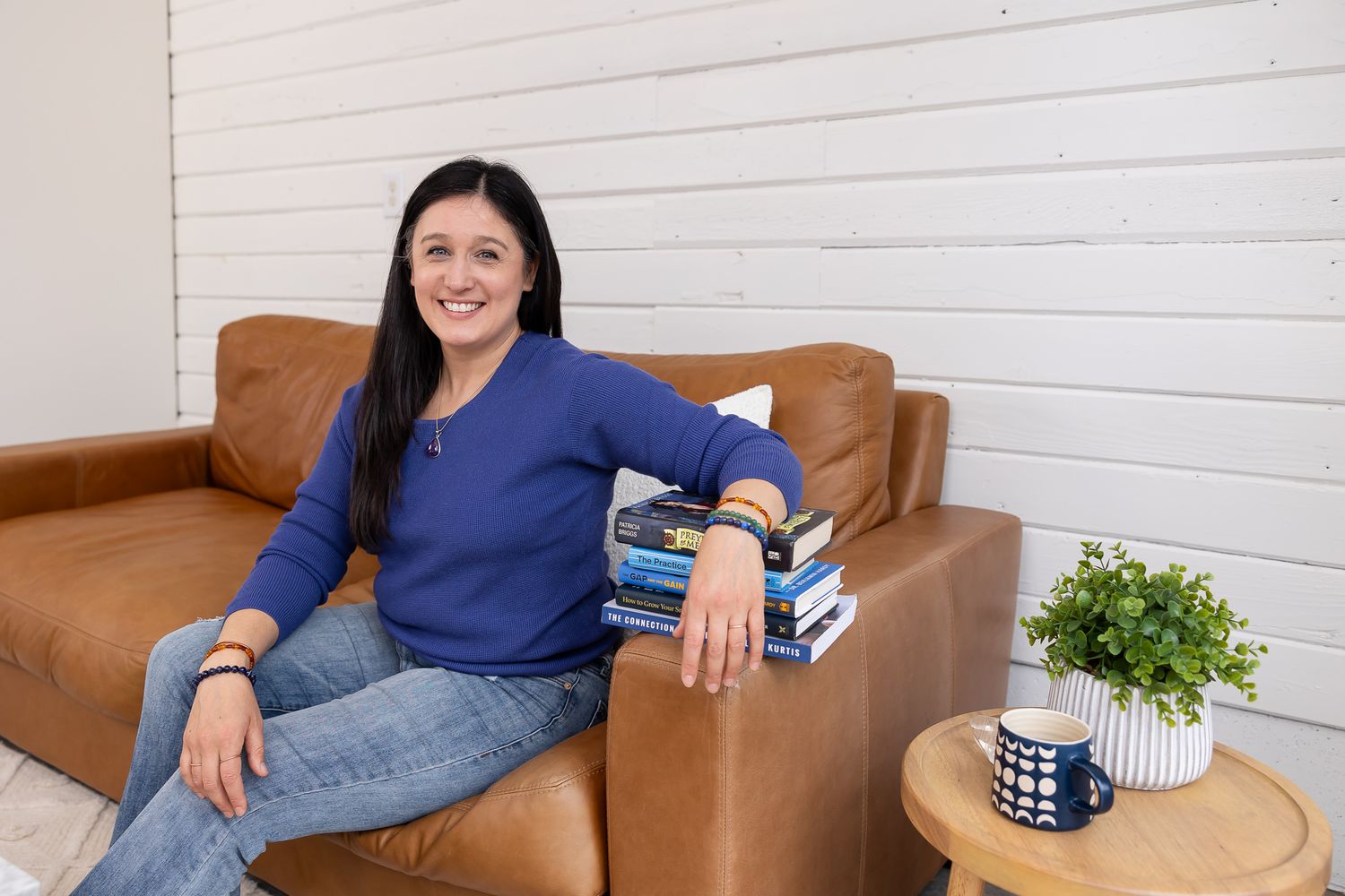 woman branding photographer sitting on couch with pile of books under arm and mug on side table for lifestyle headshot in Auburn, WA