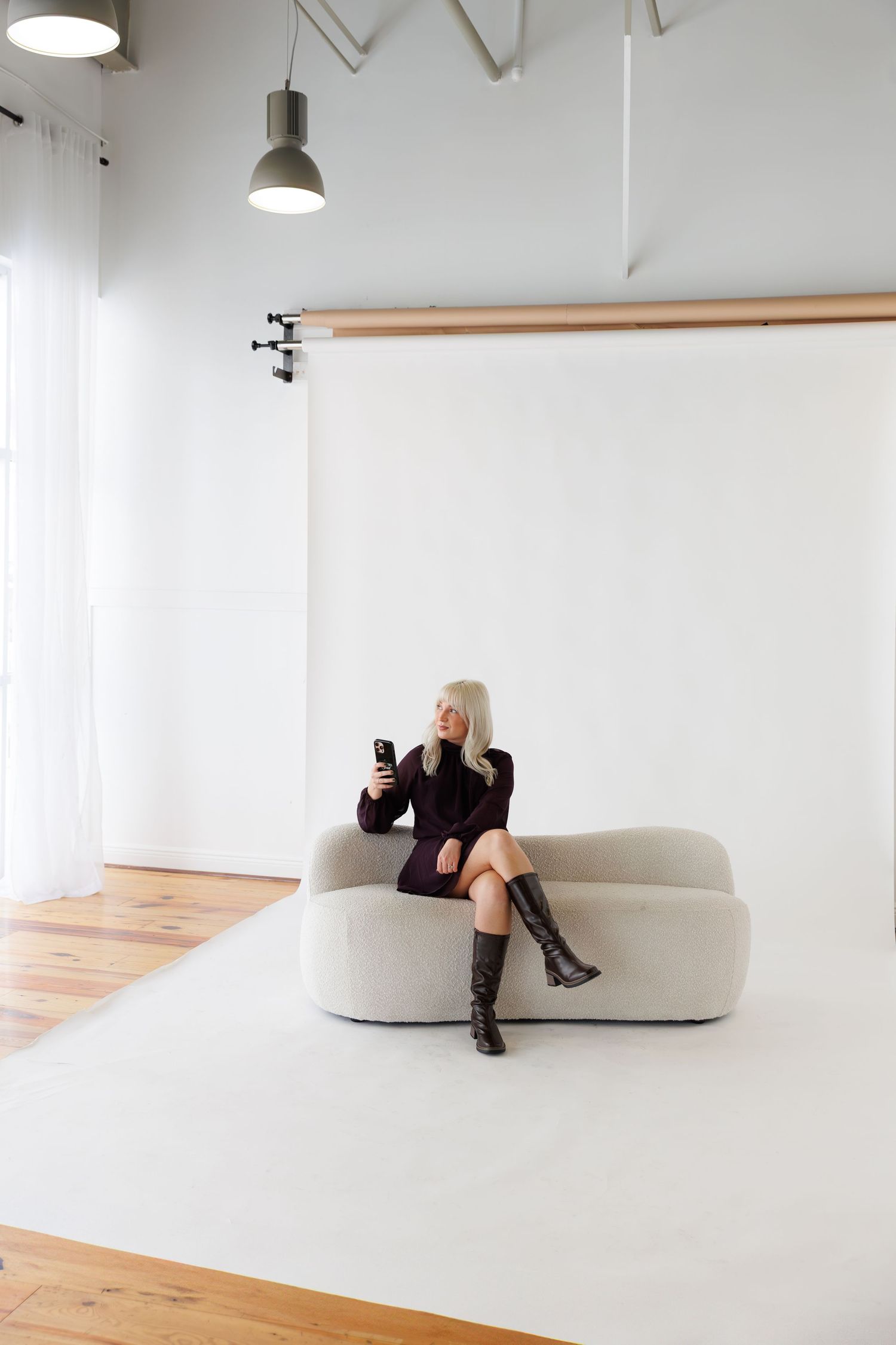 Person in white outfit lying on floor listening to vinyl records on turntable in minimalist setting.