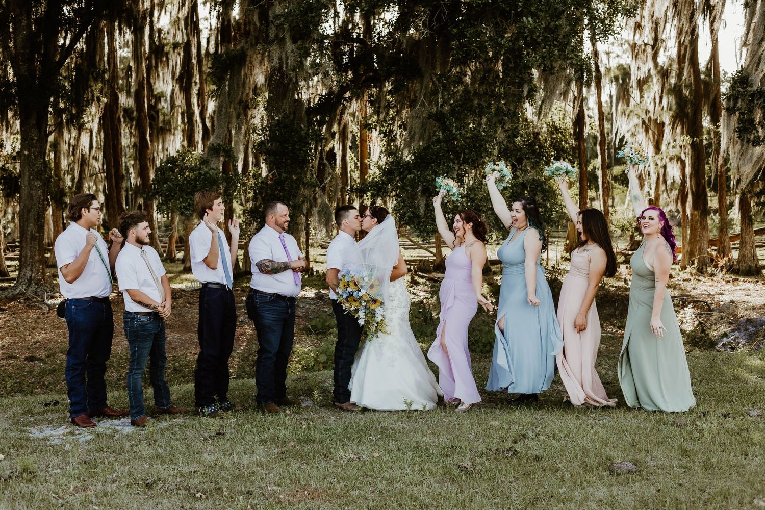 Wedding party walking and posing together outdoors beneath beautiful tree canopy in navy blue and white attire. orange bridesmaid dresses