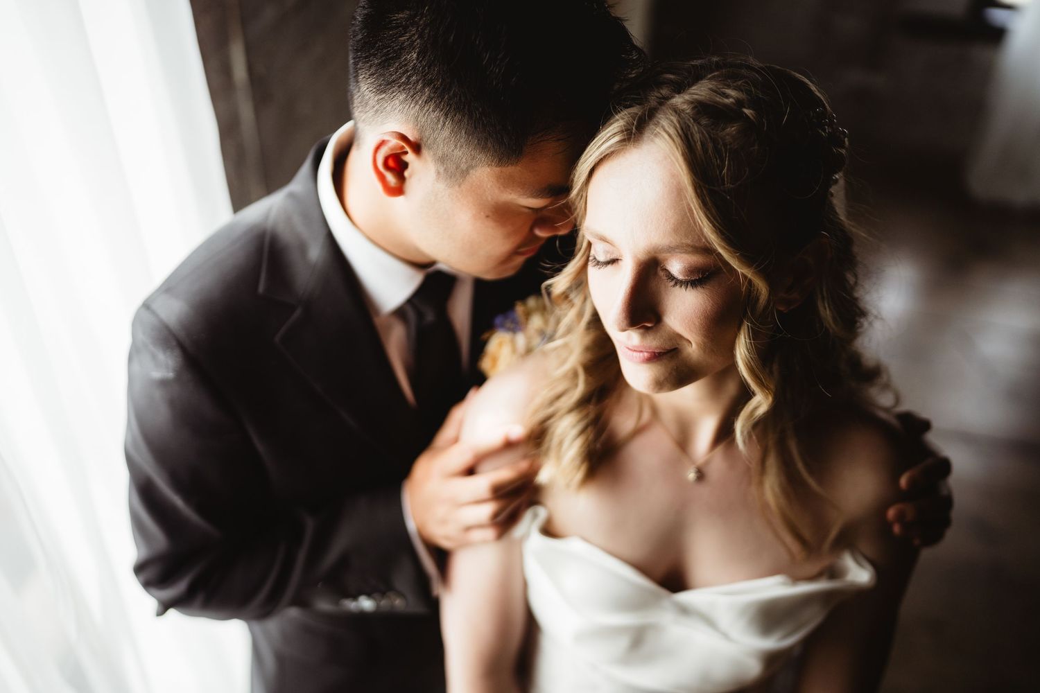 A couple in wedding attire embraces in a lush garden setting framed by soft green foliage.