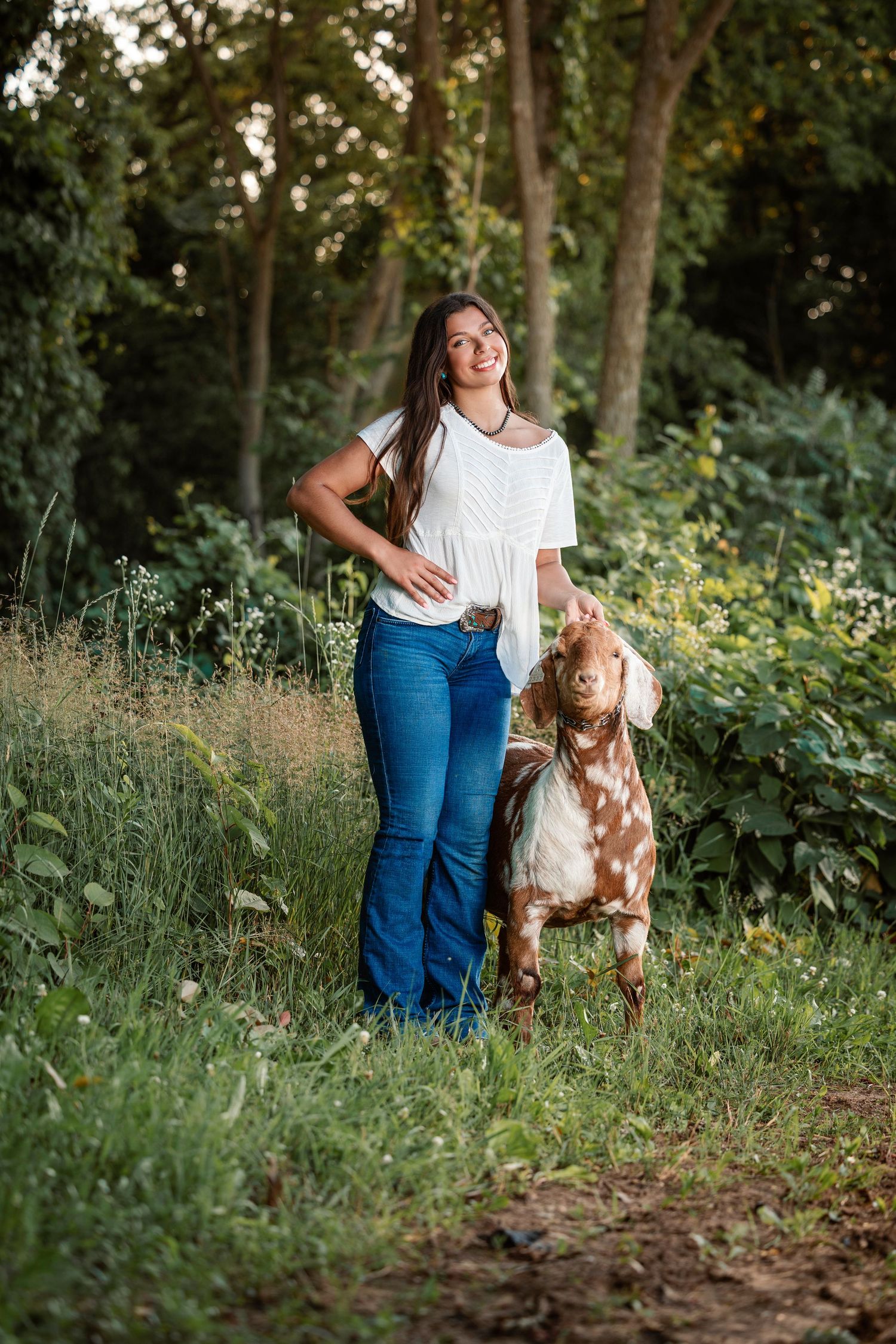 Taylor smiling while holding her goat in a sunlit pasture in Berrien County, MIchigan