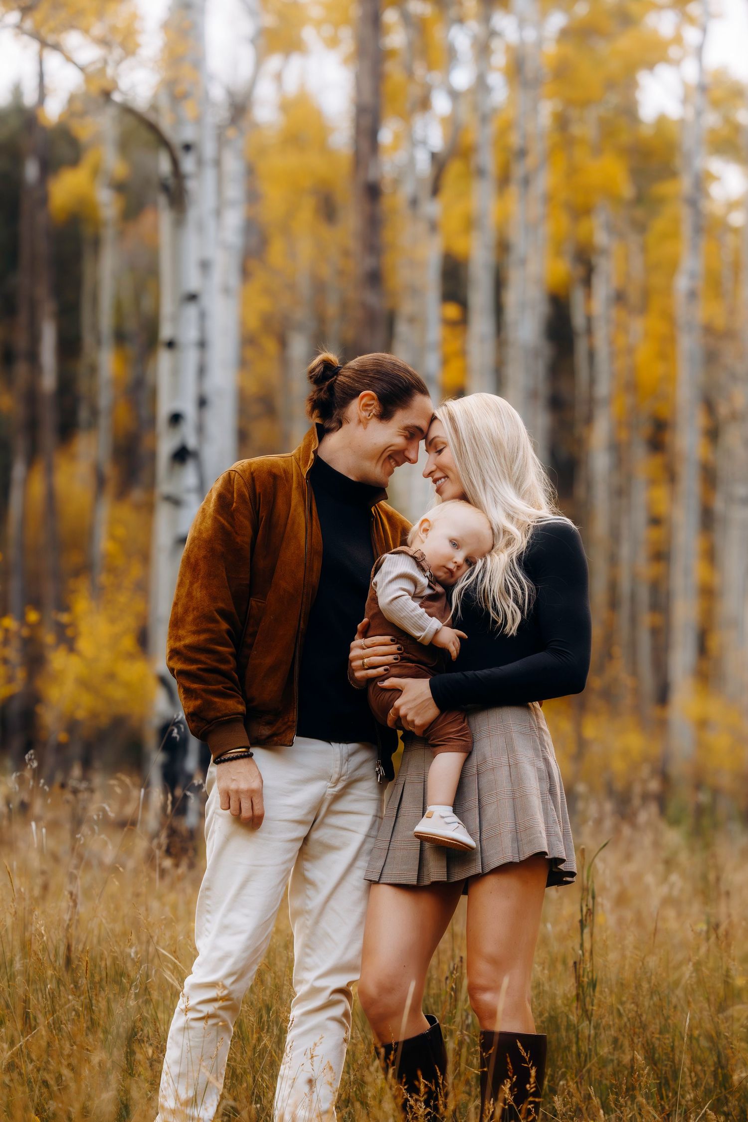 Young family with baby sharing a tender moment among golden aspen trees in autumn.