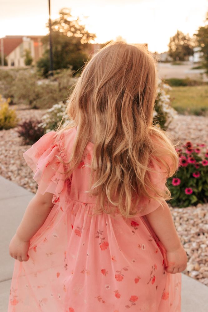 Westminster family photographer captures blonde child exploring sunlit garden path in coral dress, timeless childhood moment
