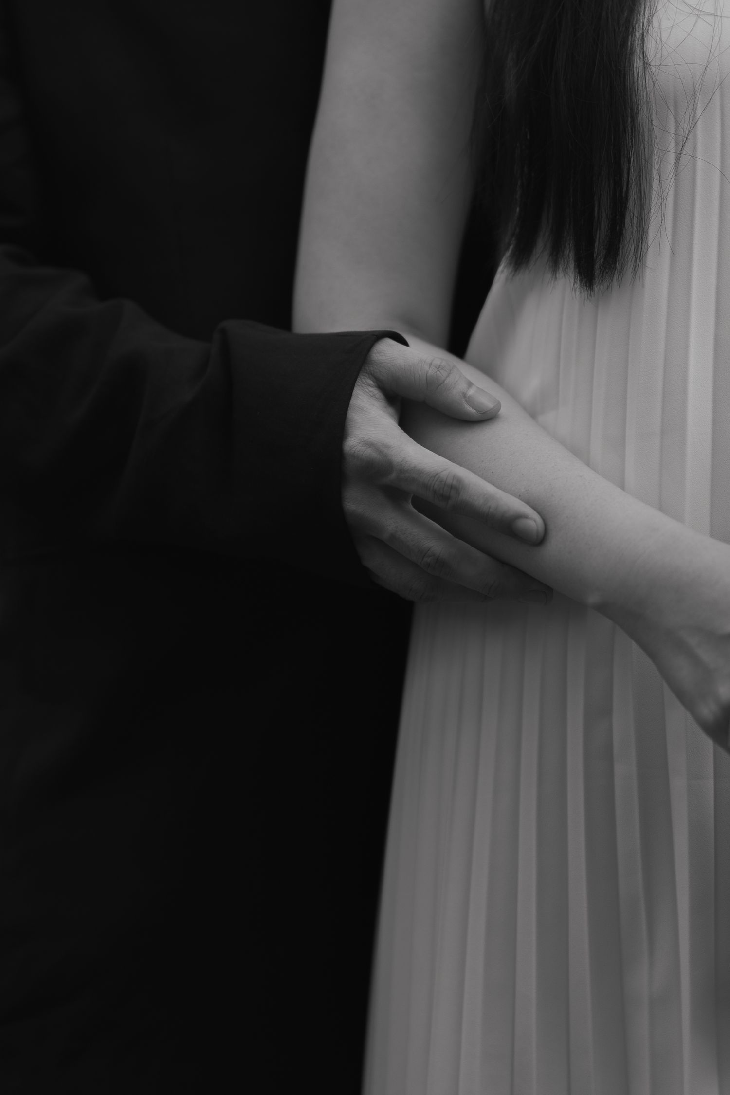 Black and white photo of a couple holding hands, man in dark suit and woman in pleated white dress.