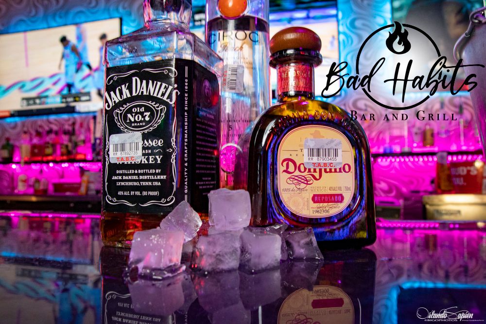 Colorful neon-lit bar display showcasing various liquor bottles including Jack Daniels and Don Julio against a vibrant purple backdrop.