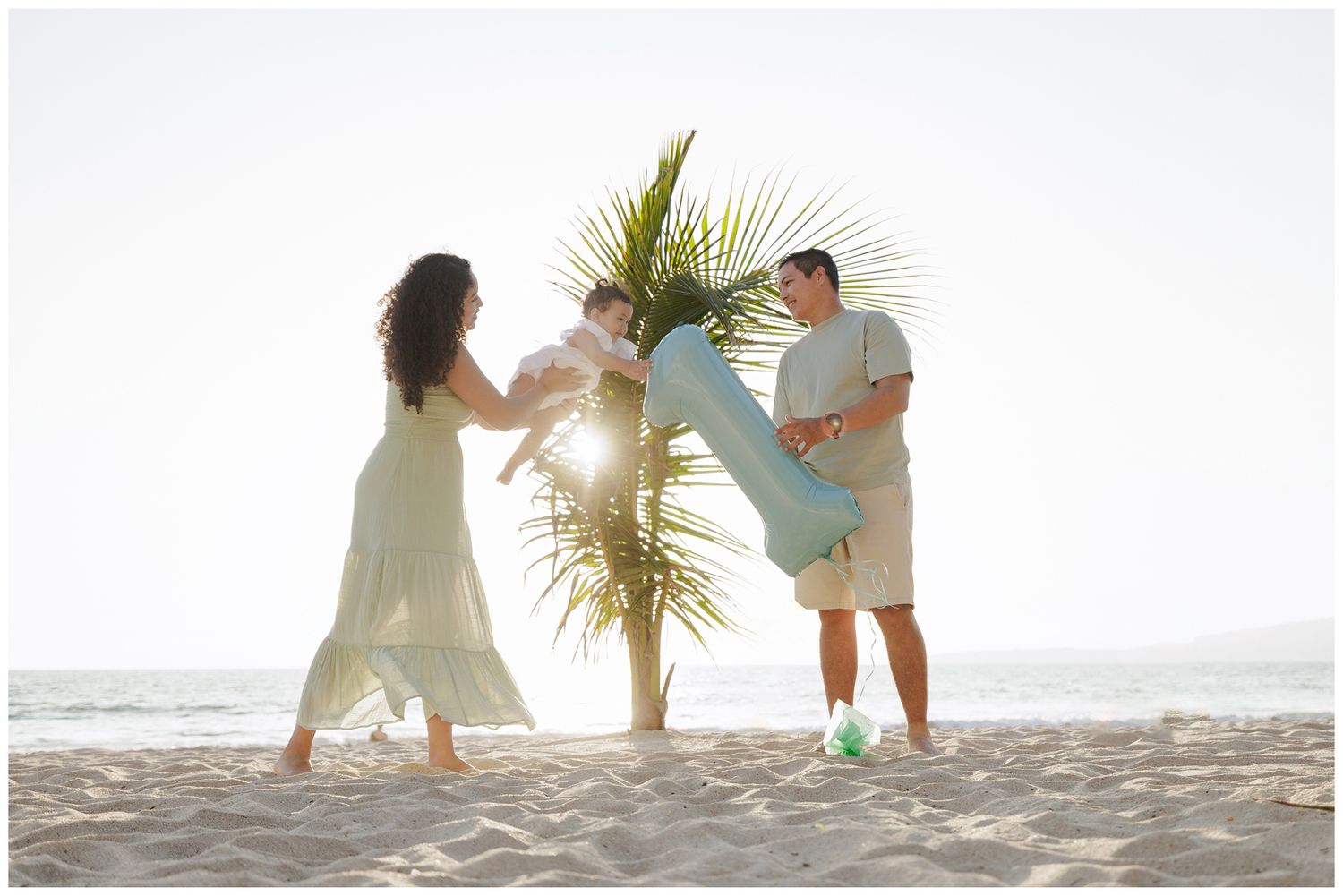 A family plays together on a beach, lifting a child in the air while wearing white clothing in black and white photography.