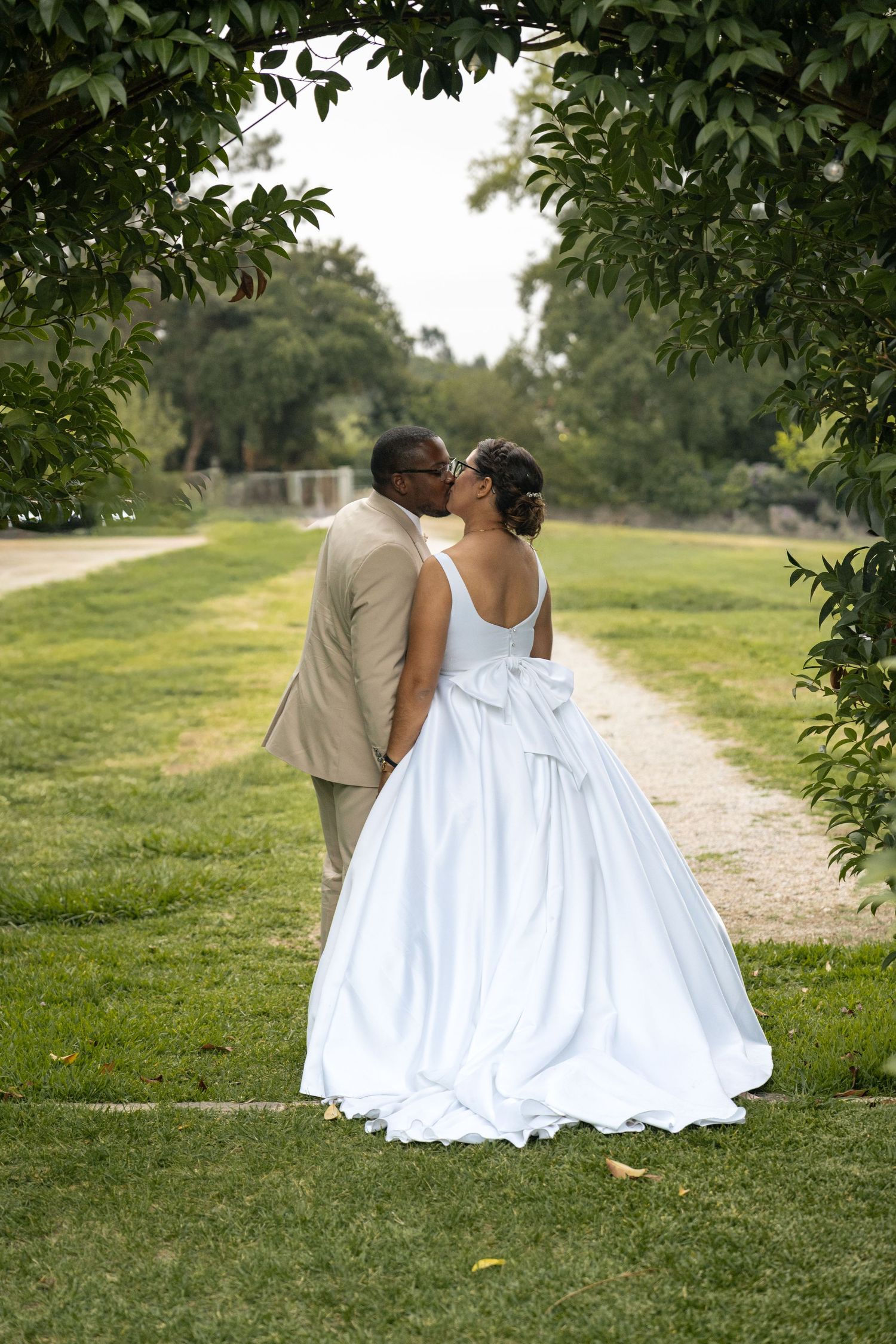 A romantic wedding couple shares a tender moment on a garden path framed by lush greenery.