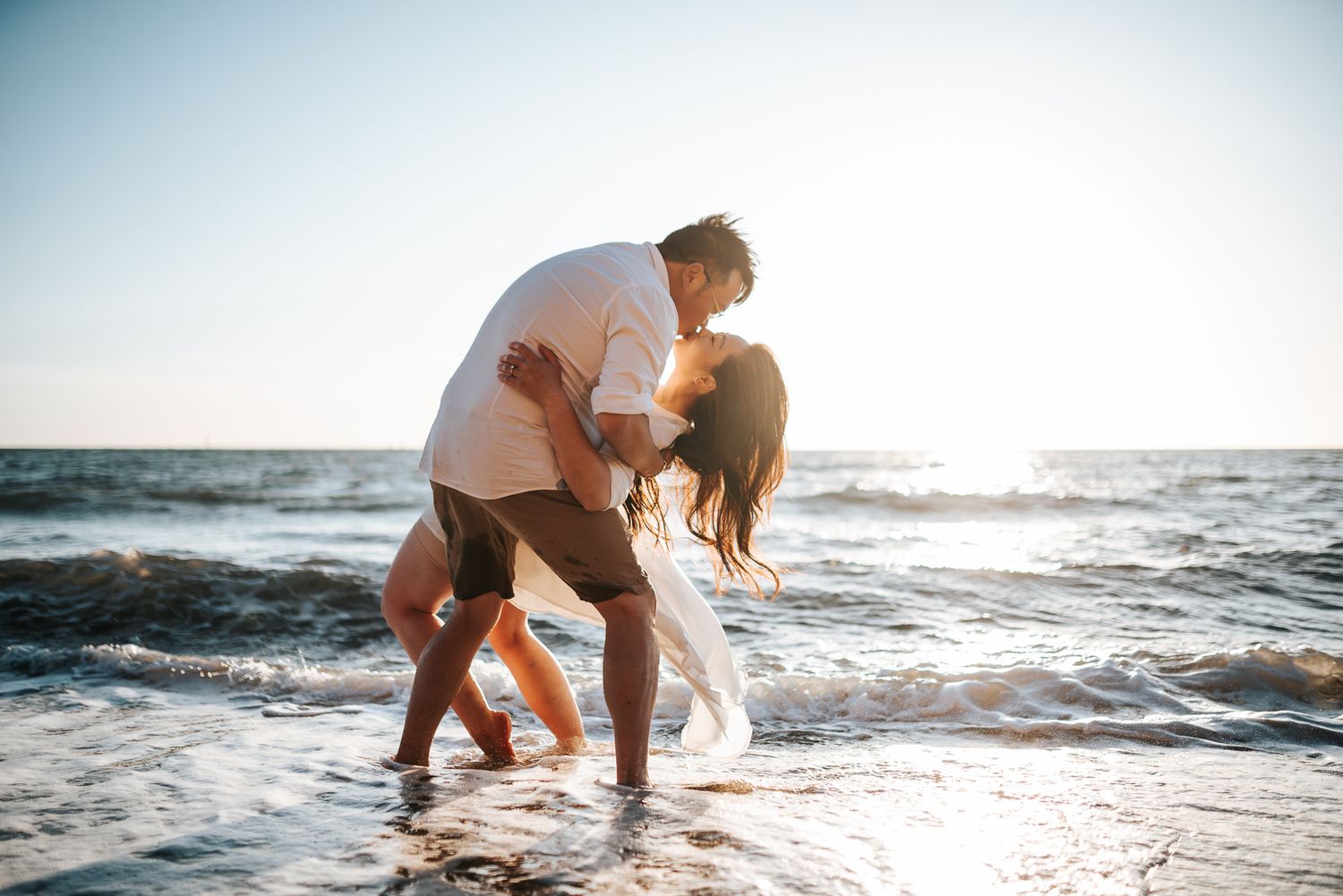 An engaged couple kissing at the beach during a golden sunset by the ocean waves taken by Melbourne couples photographer
