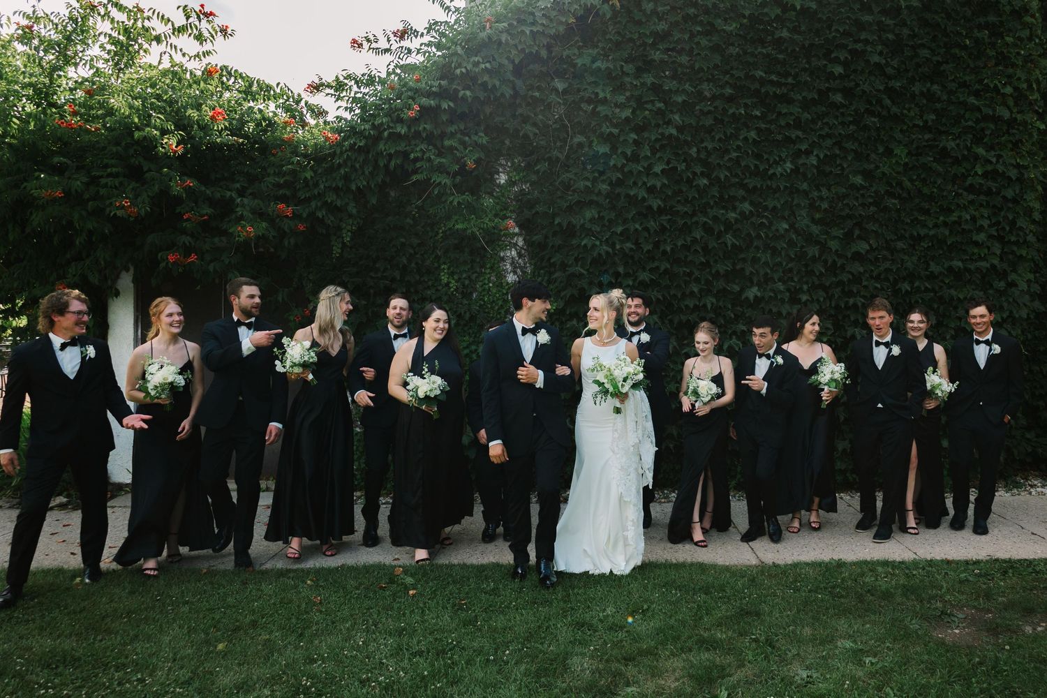 Wedding party stands in line against green foliage background during outdoor summer celebration.