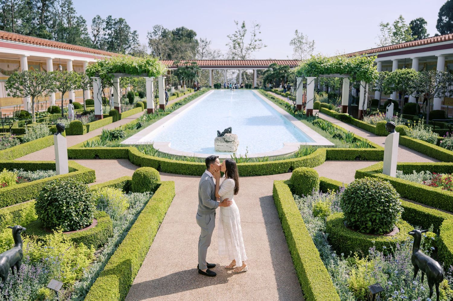 A couple embraces in the formal garden of the Getty Villa with its manicured hedges and central reflecting pool.