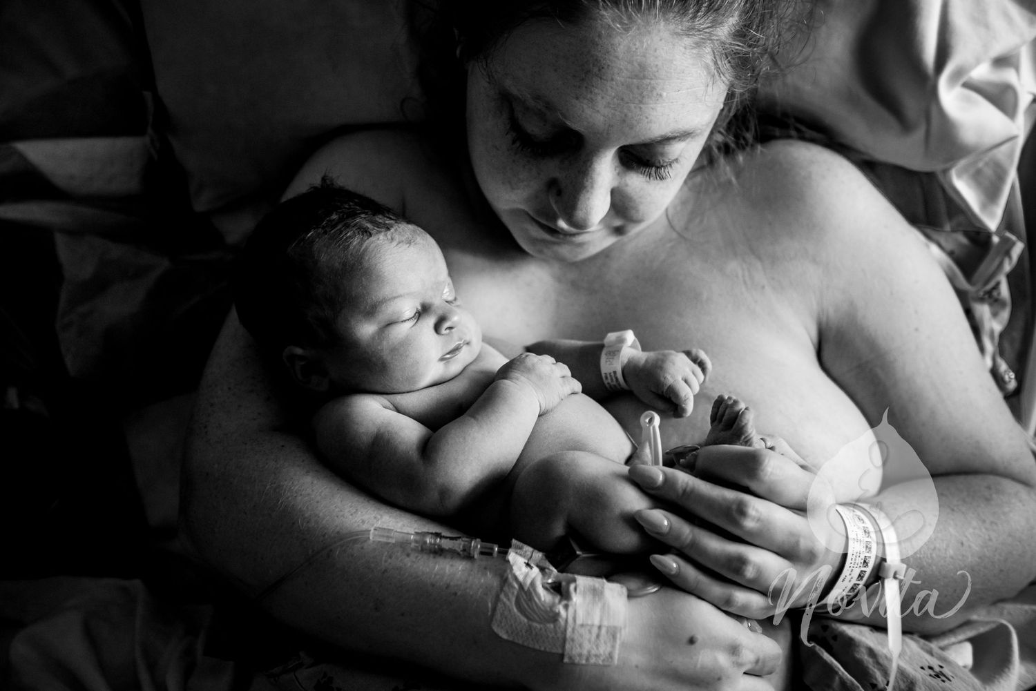 A tender moment of skin-to-skin contact between mother and newborn in black and white.