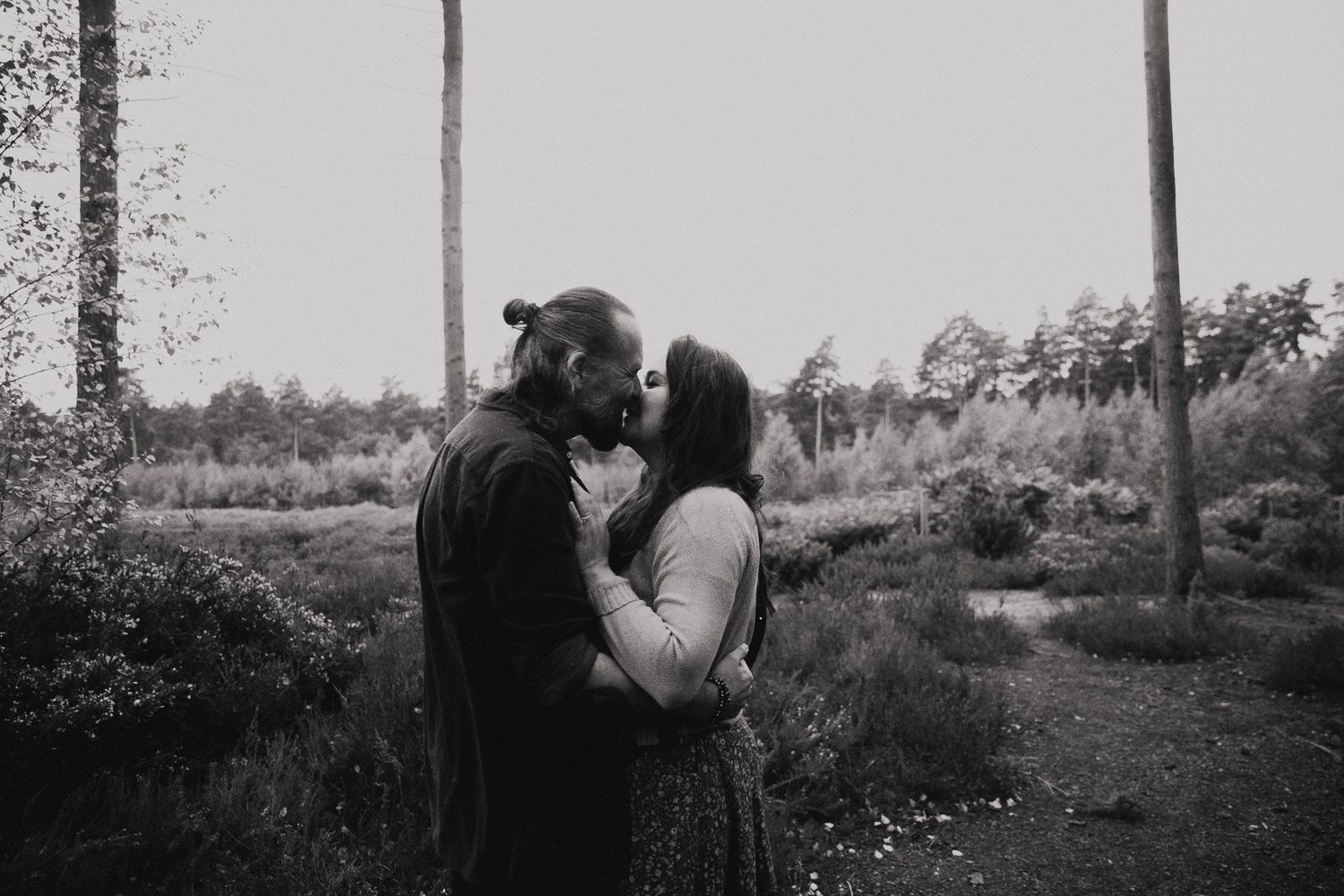 A romantic black and white photo of a couple sharing an intimate kiss in a wooded outdoor setting.