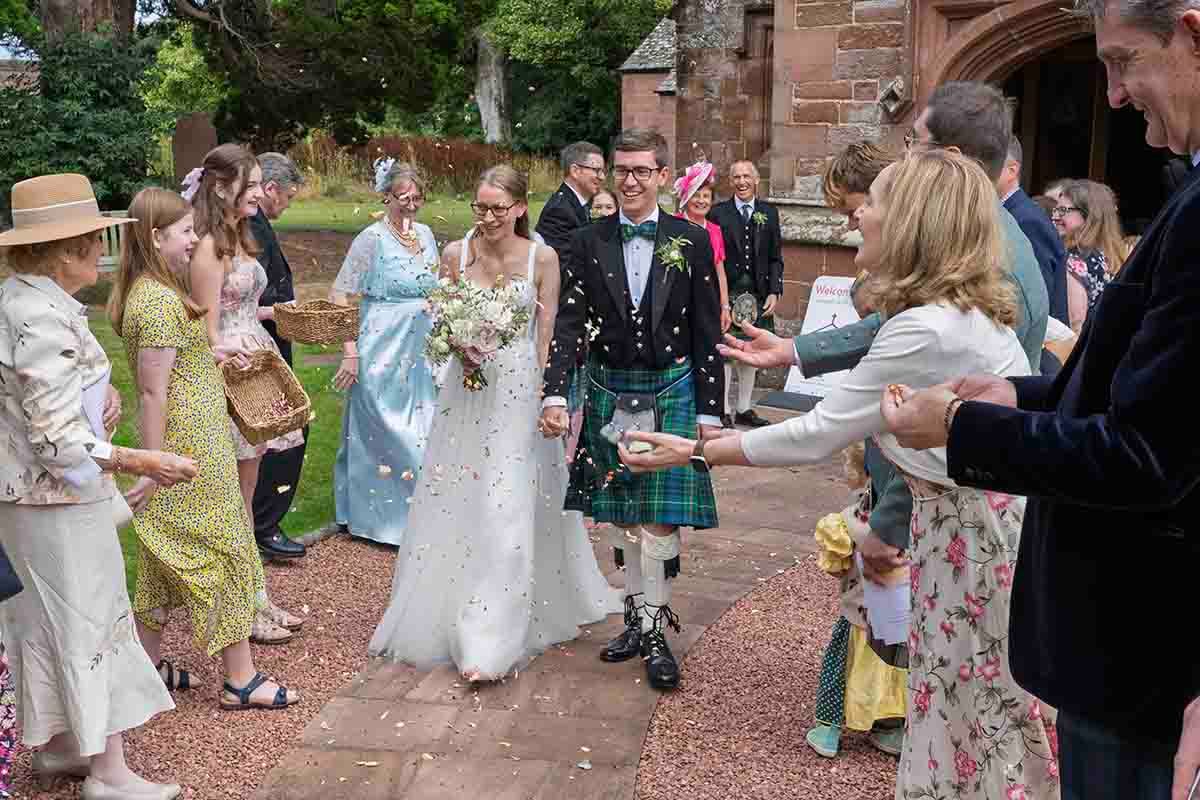 bride and groom walk through a tunnel of confetti at Wetheral church whilst having their natural wedding photography taken