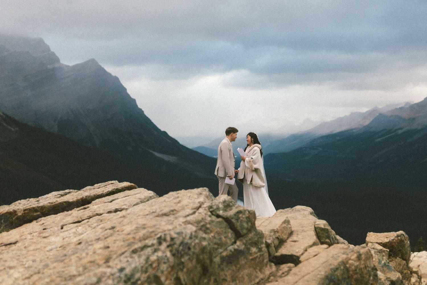 bride reads vows from a white notebook during Peyto Lake Elopement in Banff National Park with mountain peaks behind