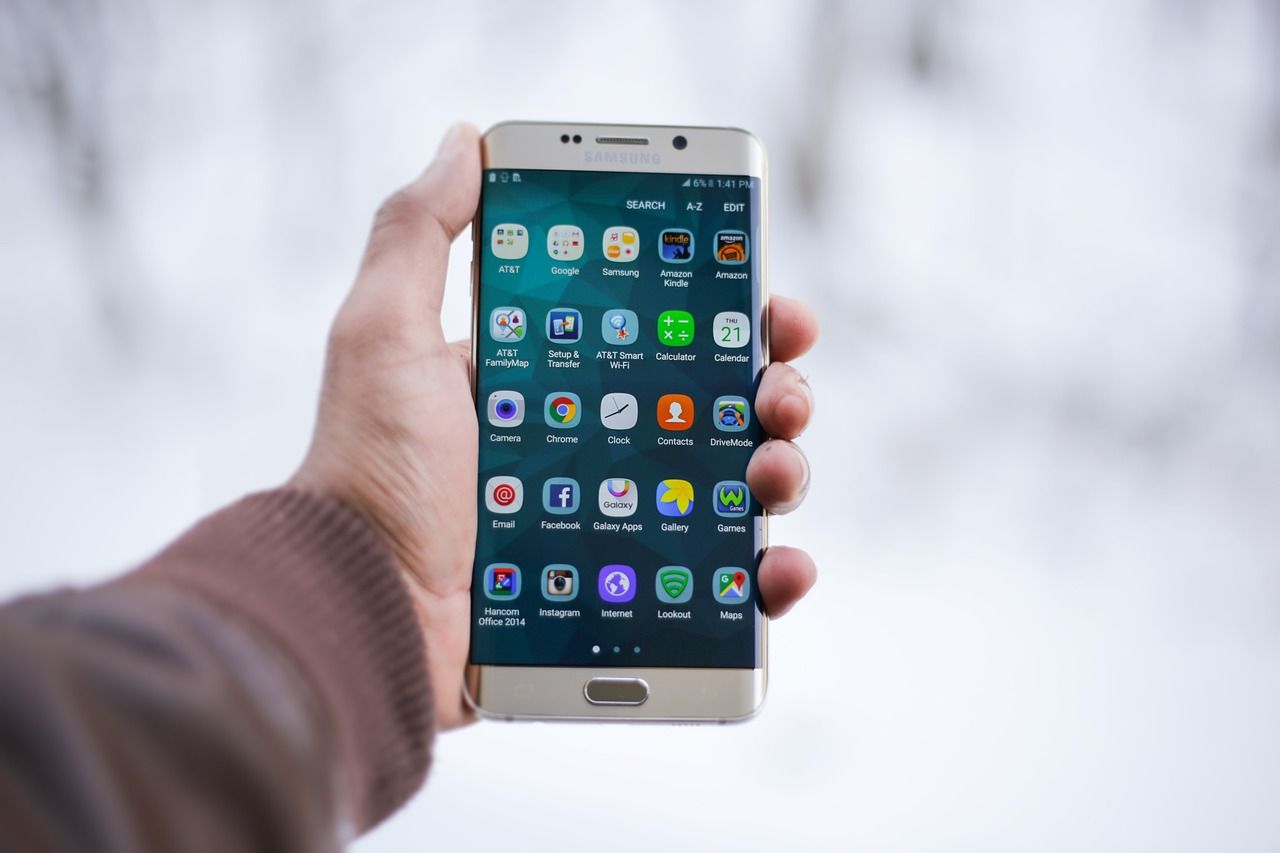 Hand holding Samsung smartphone displaying home screen with various app icons.