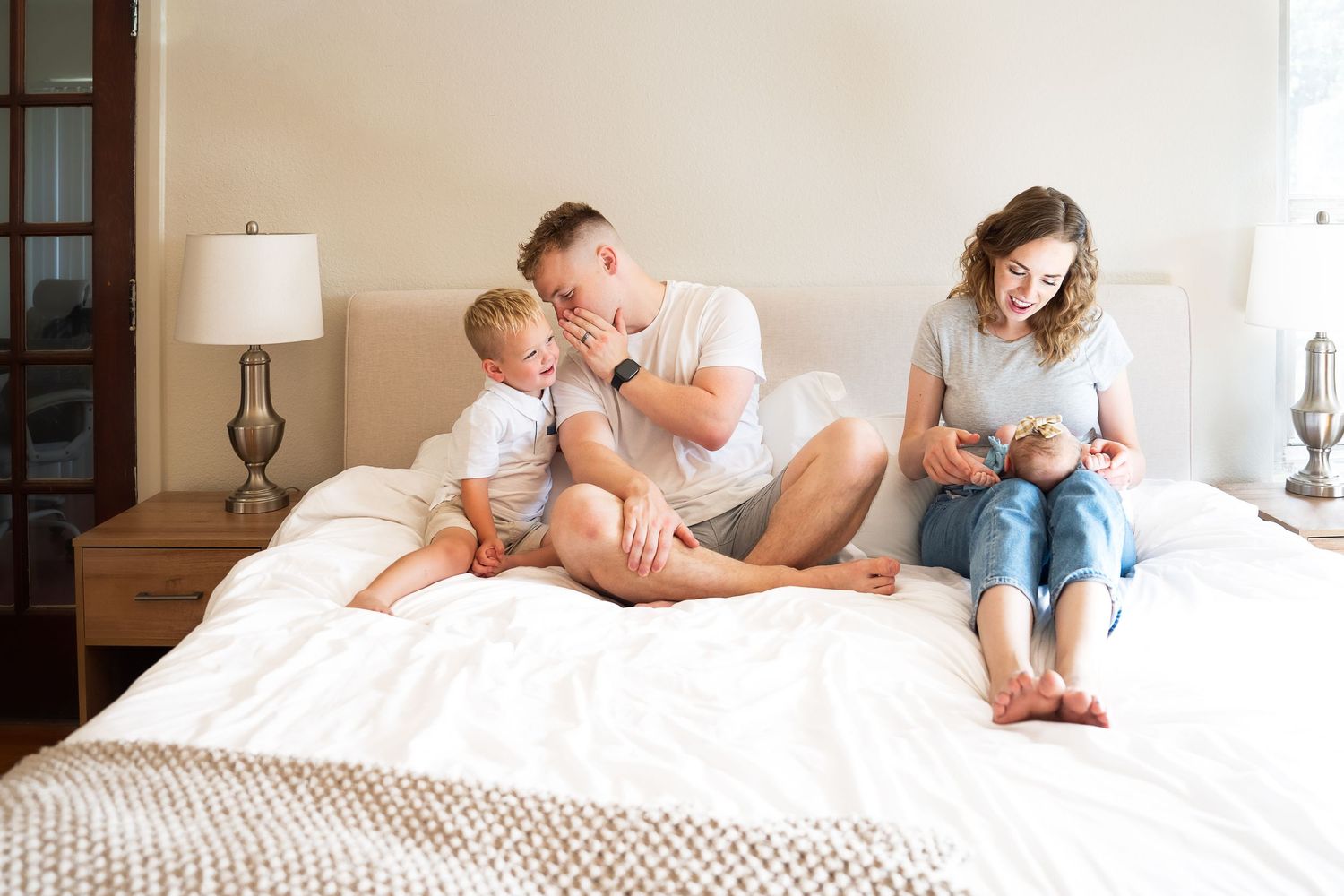 In home portrait session San Antonio Texas mother, father, toddler son and new born baby sitting on bed